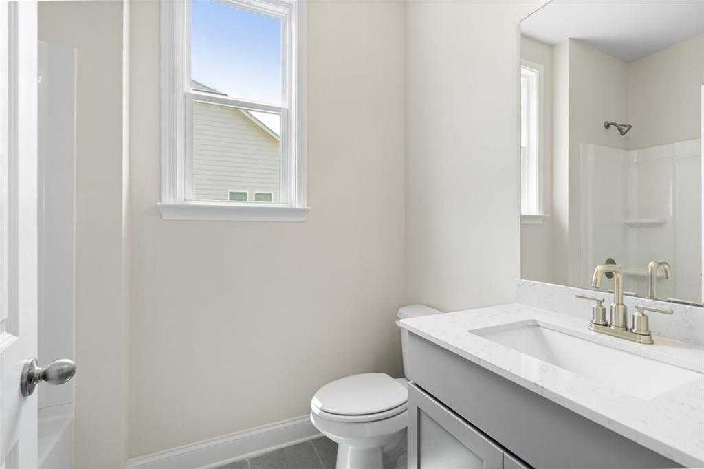 Modern bathroom with white quartz vanity, gold fixtures, tiled shower, and window view in Davidson Homes The Willow D at Wehunt Meadows, Hoschton