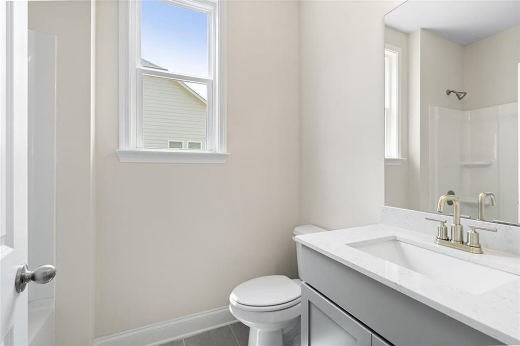 Modern bathroom with white quartz vanity, gold fixtures, tiled shower, and window view in Davidson Homes The Willow D at Wehunt Meadows, Hoschton