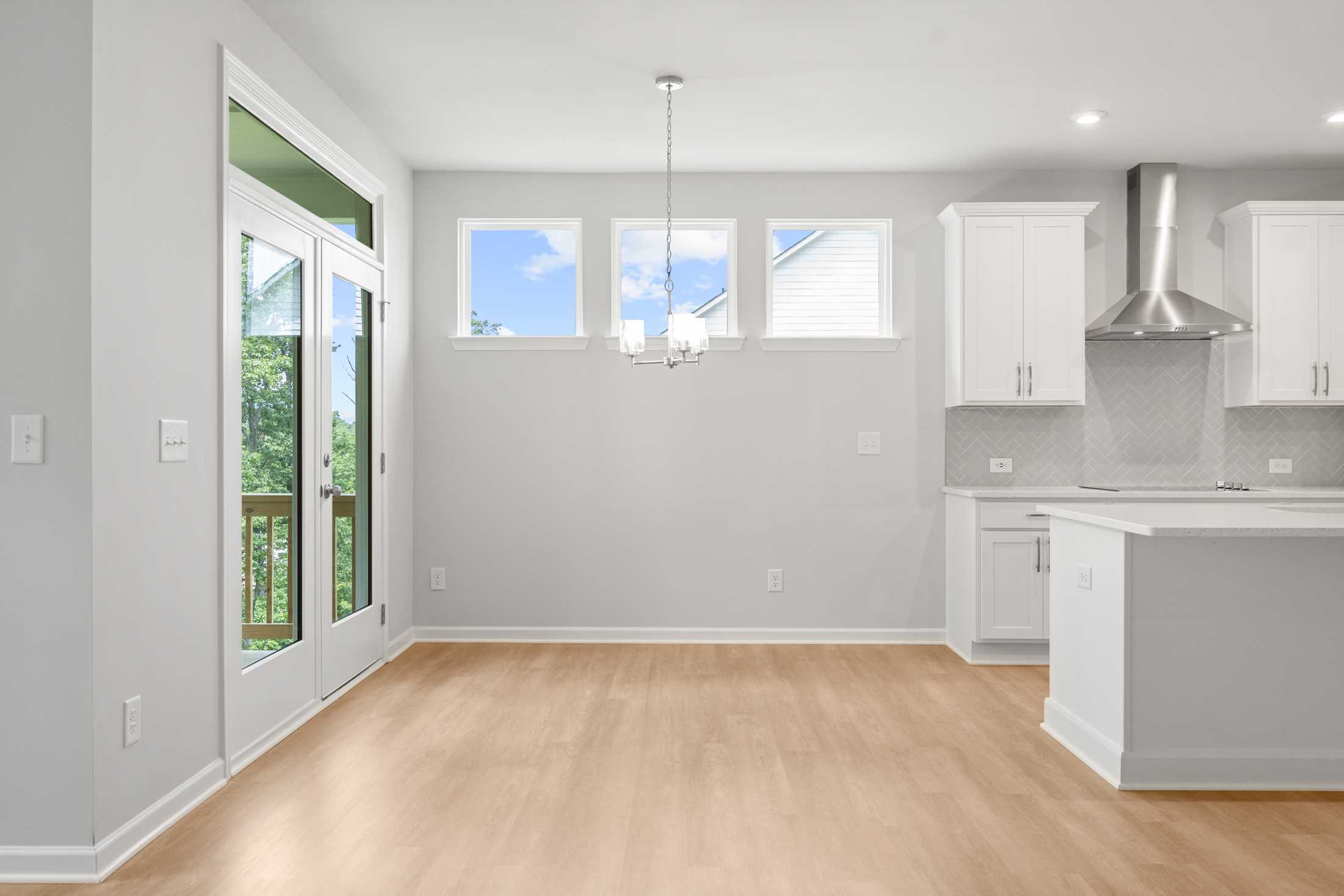 Spacious kitchen and dining area in The Ash B at Wehunt Meadows with white cabinetry, large island, hardwood floors, and French doors to deck