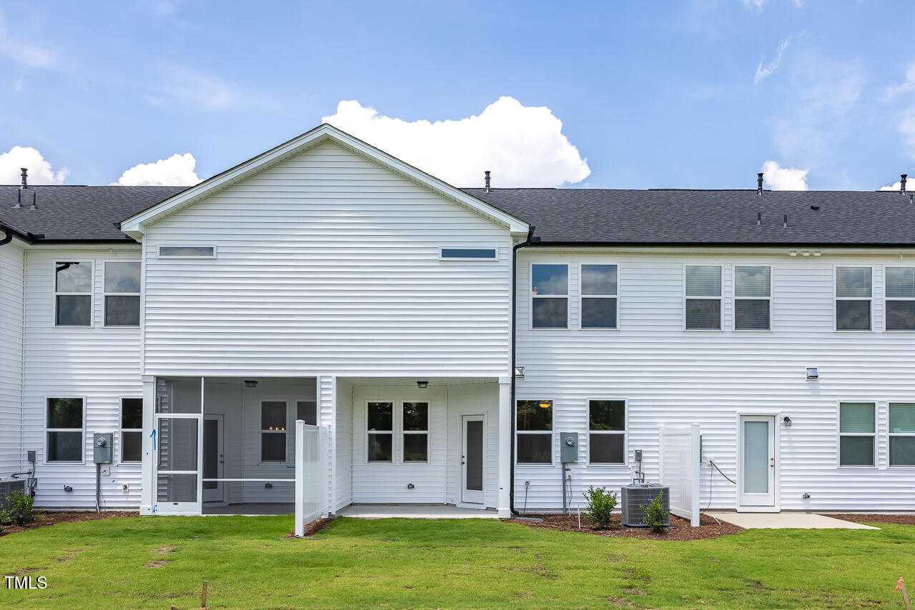 Rear view of two-story white home with screened porch, back door, and lush green backyard in Springvale, Fuquay-Varina, NC