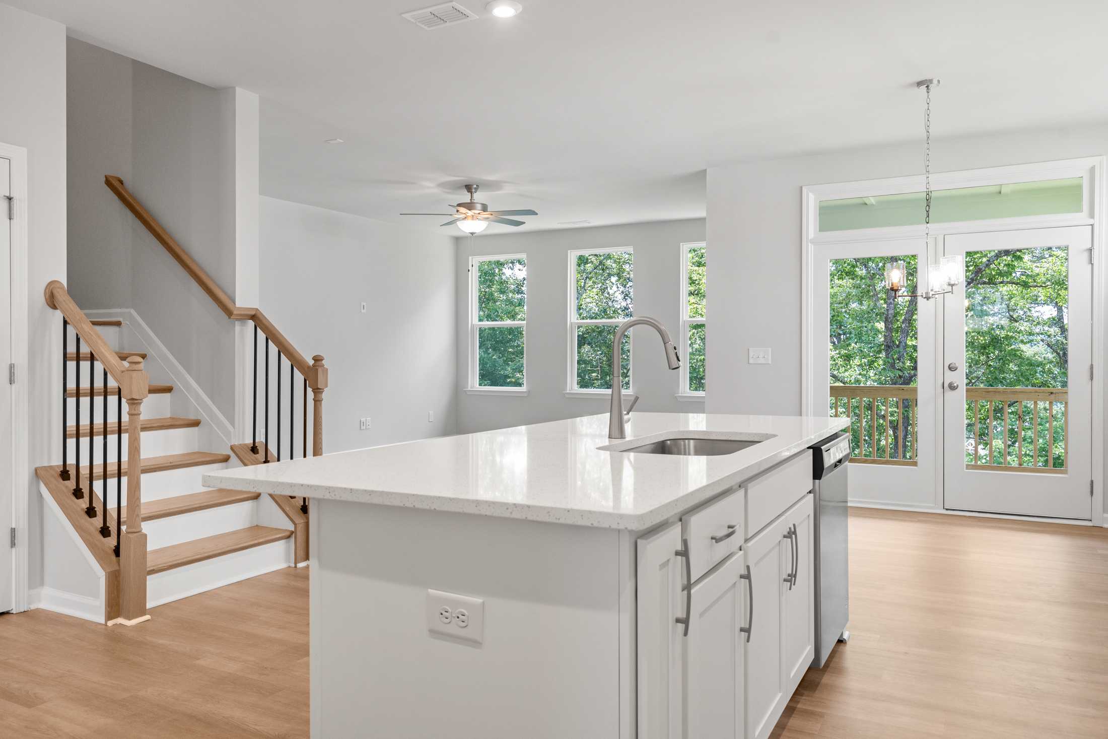 Spacious open-concept kitchen in The Ash B featuring white quartz island, stainless sink, hardwood floors, and staircase to second floor