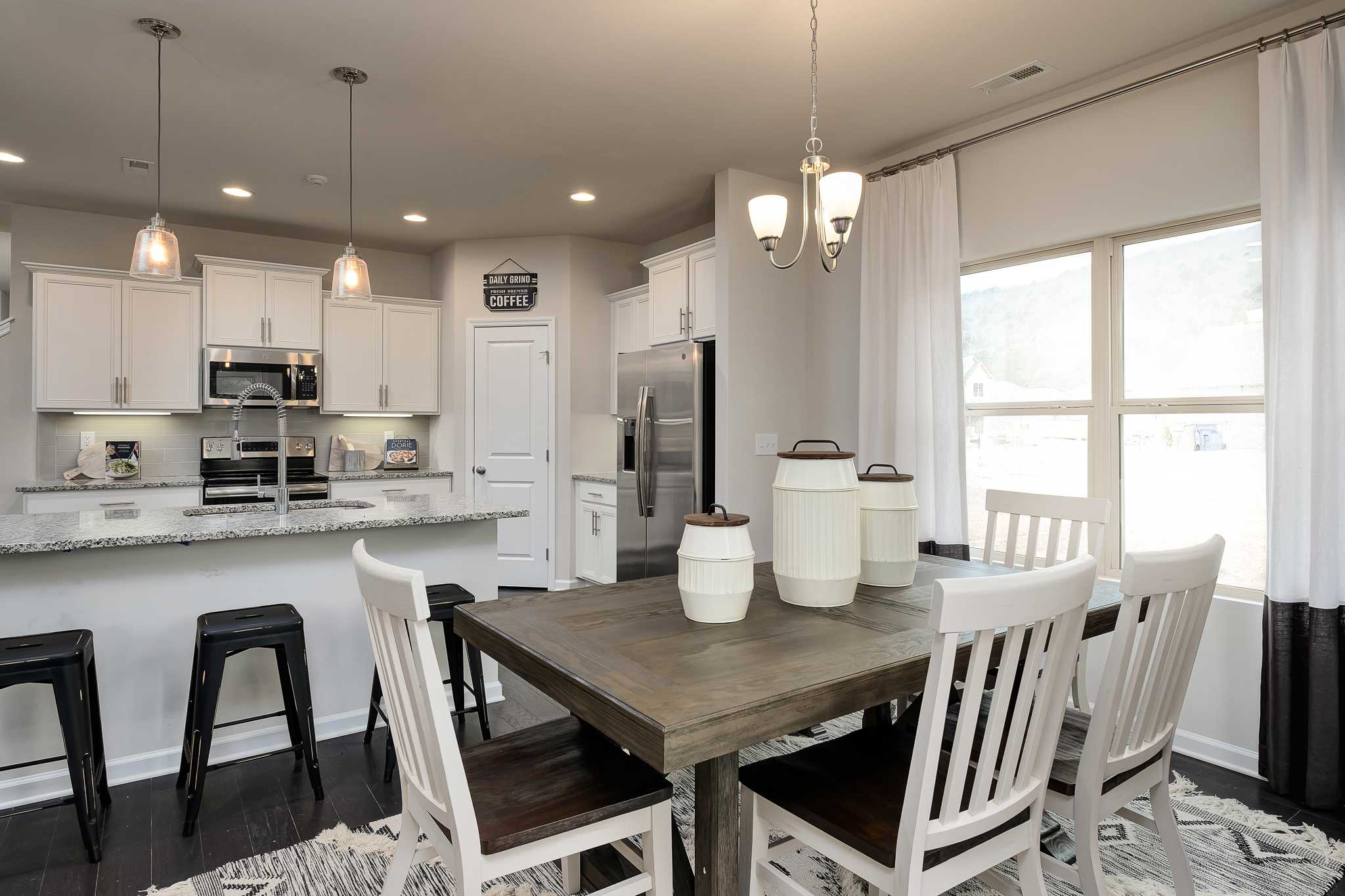 Spacious open-concept kitchen and dining area at The Reserve at Overton in Hampton Cove AL with white cabinets, granite island, and farmhouse table