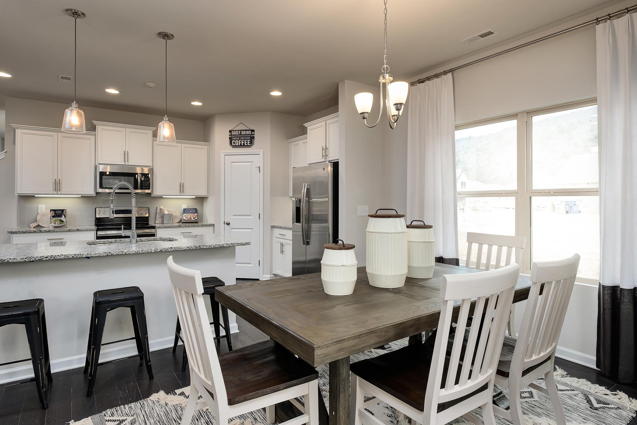 Spacious open-concept kitchen and dining area at The Reserve at Overton in Hampton Cove AL with white cabinets, granite island, and farmhouse table