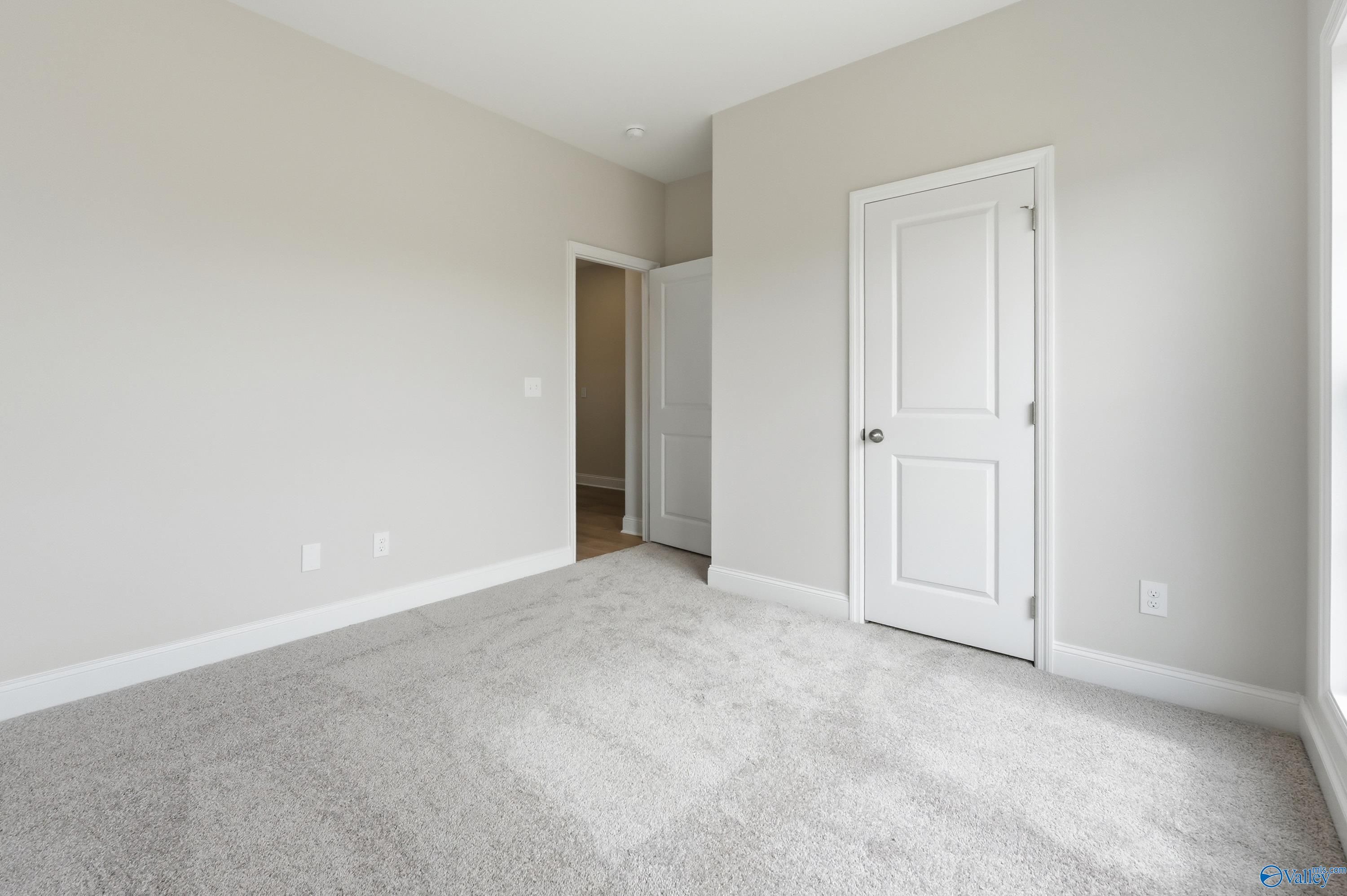 Spacious empty bedroom with beige walls, white doors, and carpet flooring in Davidson Homes The Franklin, Meridianville, AL