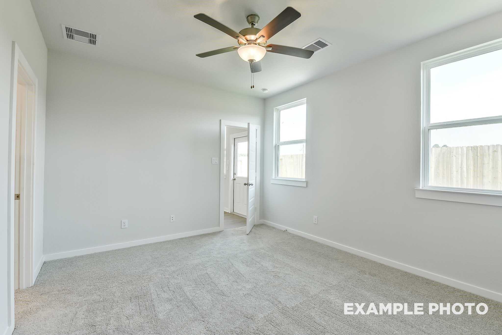 Bright secondary bedroom with ceiling fan, gray carpet, and large windows in Davidson Homes Colorado F, Conroe, Texas