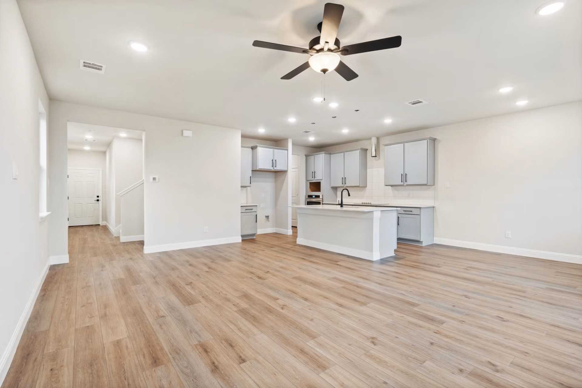 Spacious open-concept kitchen with white cabinets, central island, hardwood floors and ceiling fan in Davidson Homes The Wake D, Wylie Texas