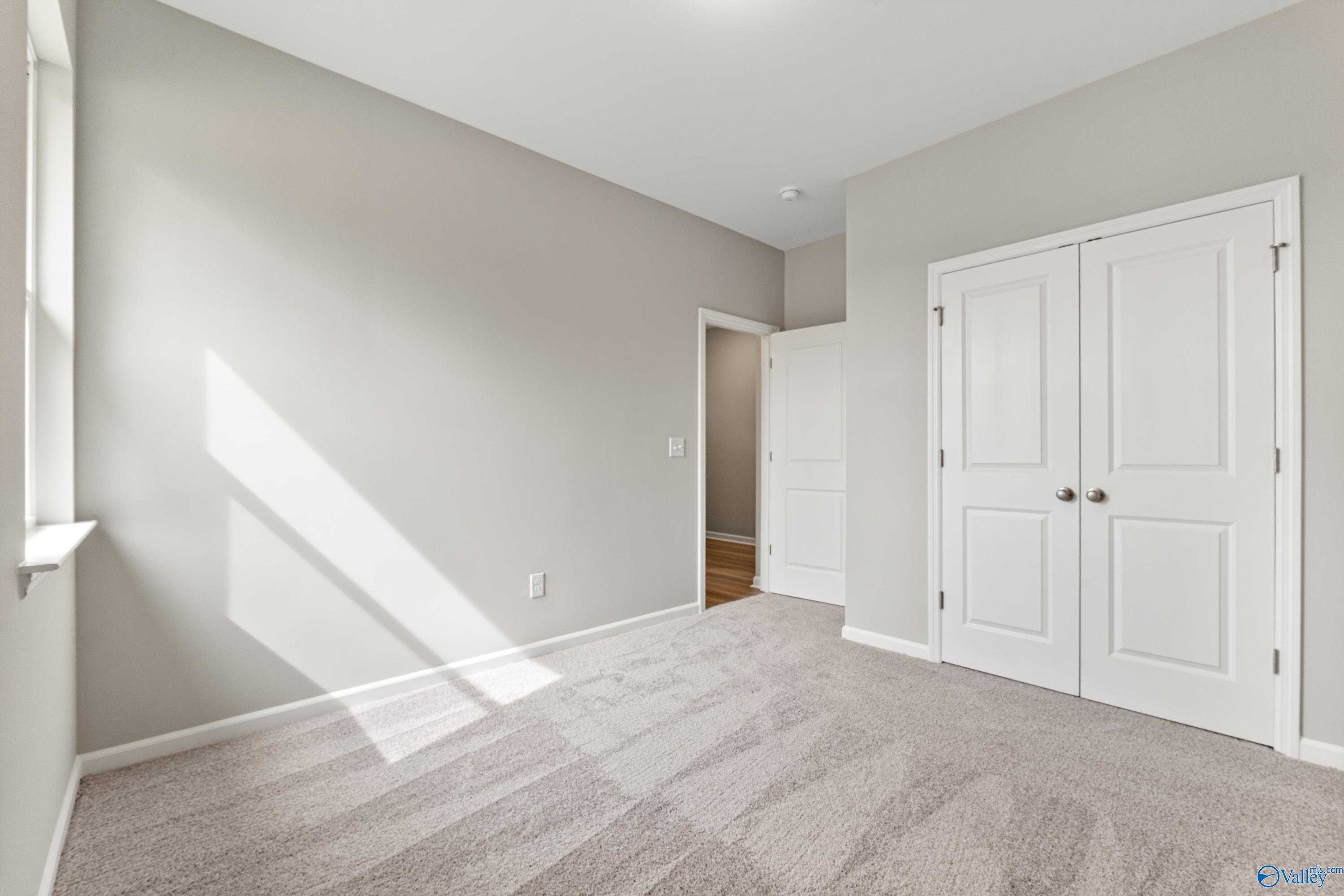 Bright secondary bedroom with light gray walls, white double closet doors, carpeted floor, and natural sunlight in Davidson Homes The Aurora, Fayetteville, TN