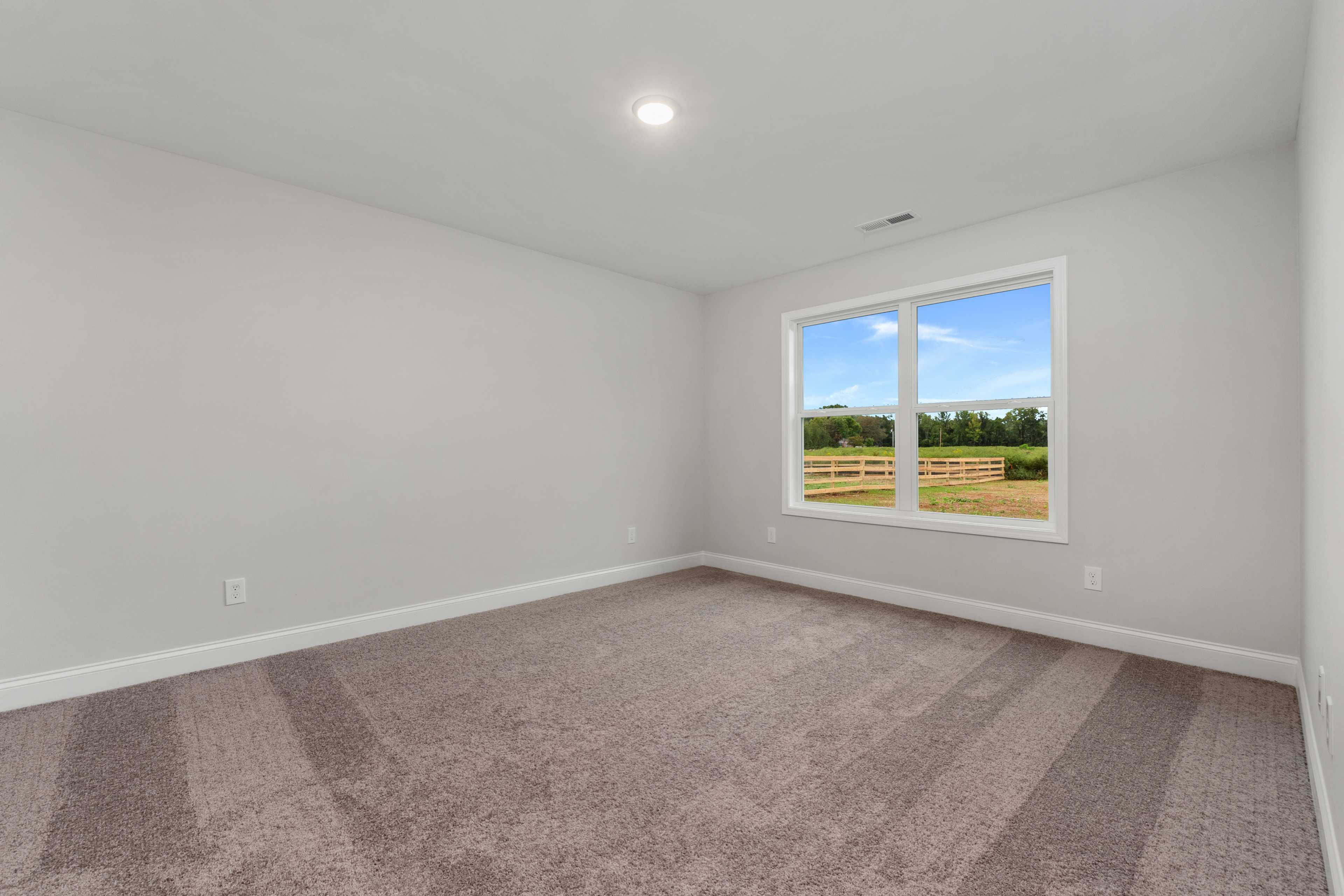 Spacious empty bedroom interior at Collins Lane in Meridianville Alabama with gray walls carpet flooring and large window overlooking green field fence