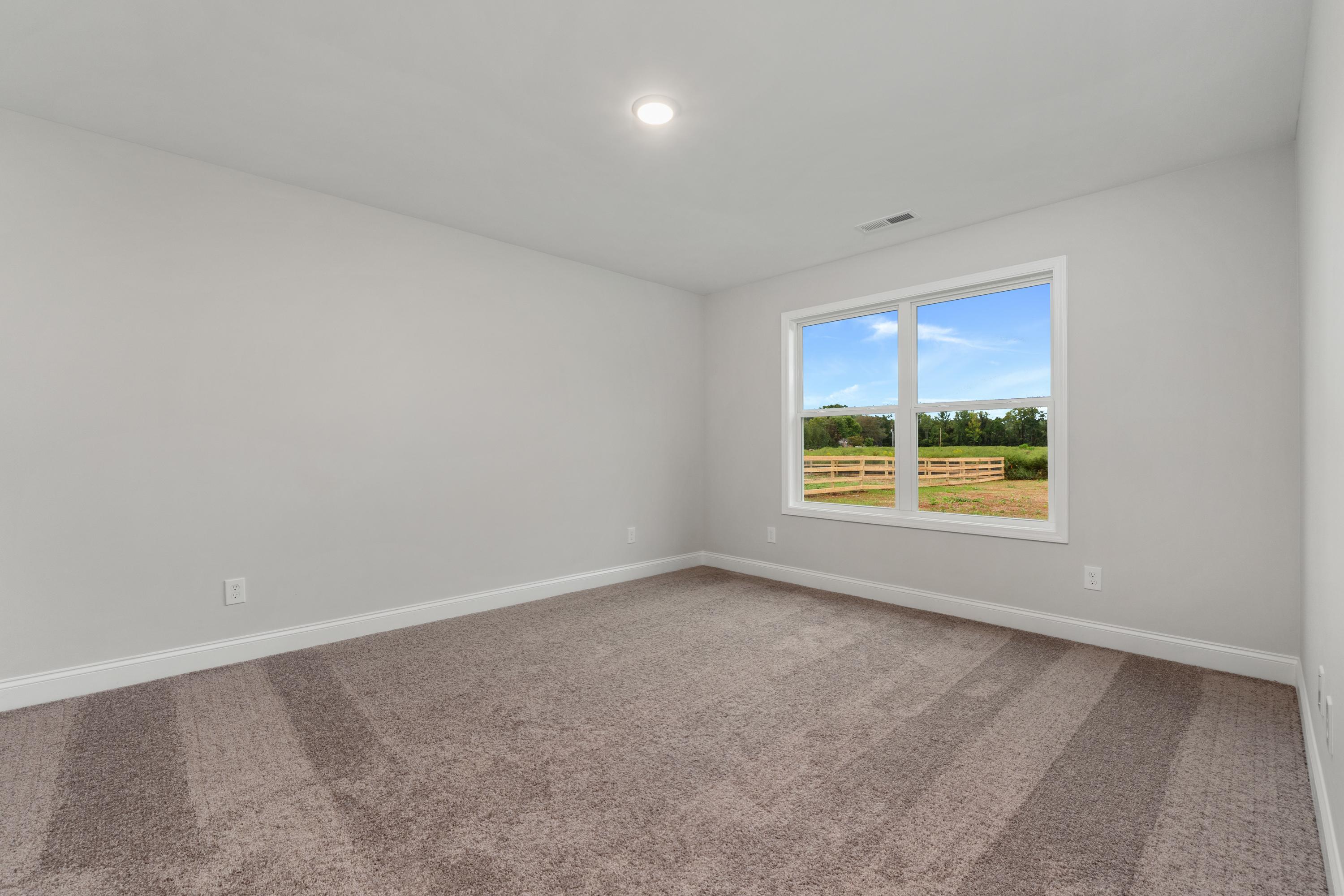 Spacious empty bedroom interior at Collins Lane in Meridianville Alabama with gray walls carpet flooring and large window overlooking green field fence