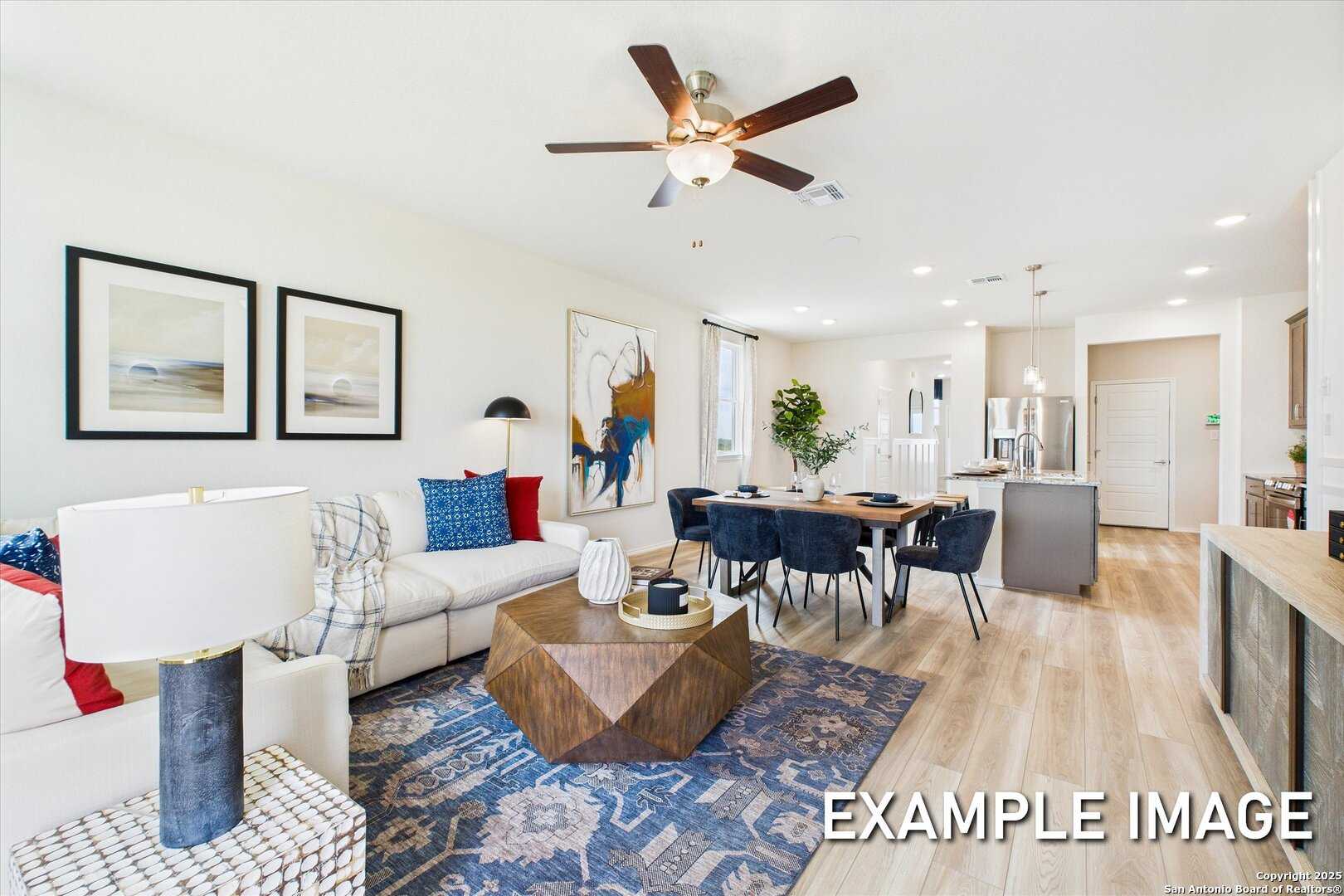 Modern open-concept living room with white sofa, abstract art, dining table, ceiling fan, and kitchen island in Davidson Homes Brazos C, San Antonio