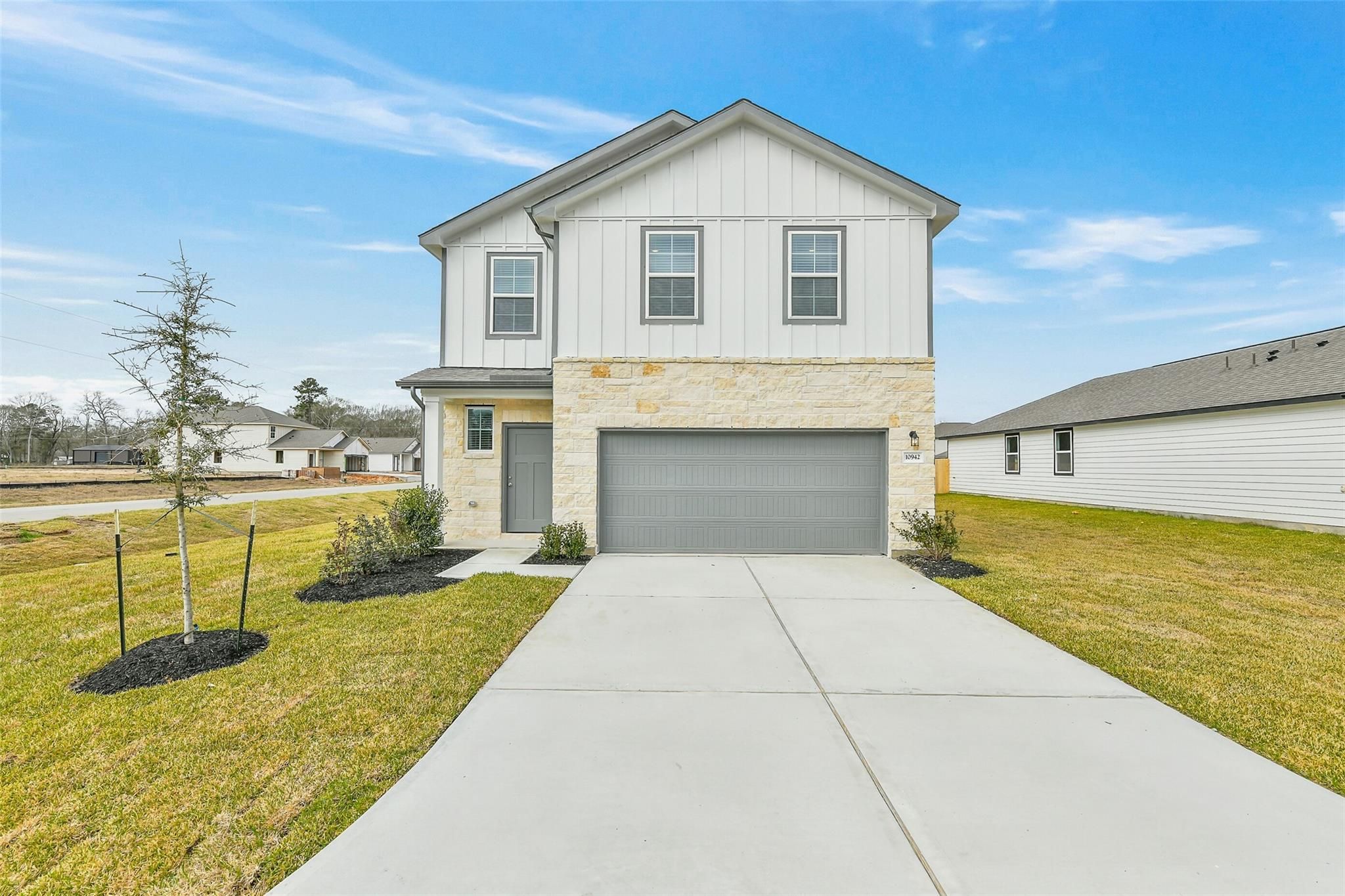 Modern two-story 5-bedroom home with white shiplap siding, beige stone accents, 2-car garage, driveway, and front yard landscaping in Liberty Estates, Cleveland, Texas