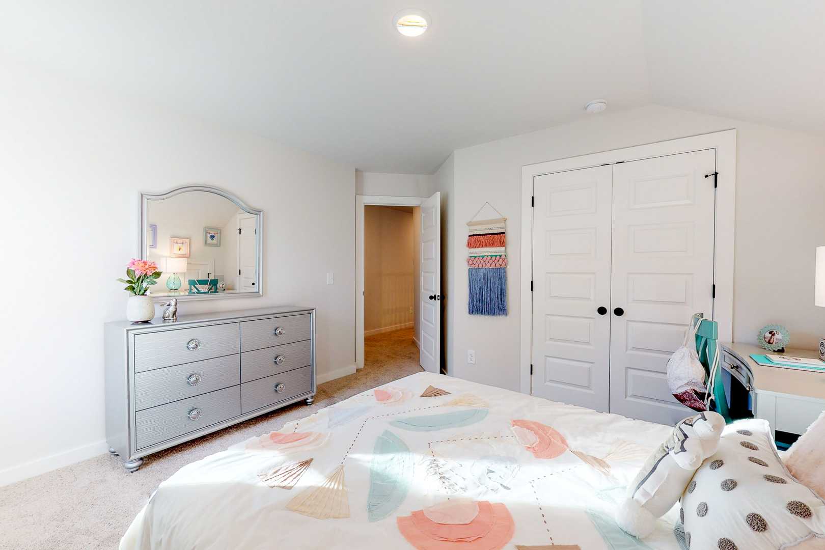 Spacious girl's bedroom at Liberty Creek in Gallatin TN with colorful bed, silver dresser, mirror, and closet doors