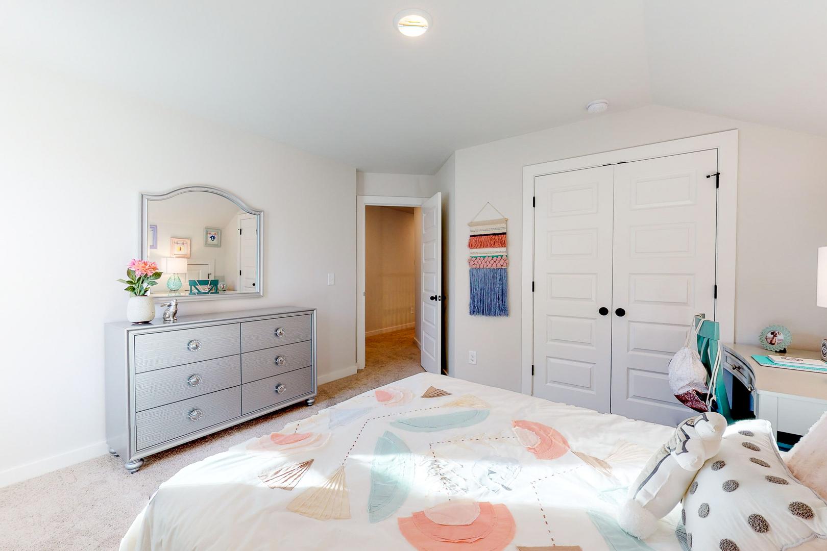 Spacious girl's bedroom at Liberty Creek in Gallatin TN with colorful bed, silver dresser, mirror, and closet doors