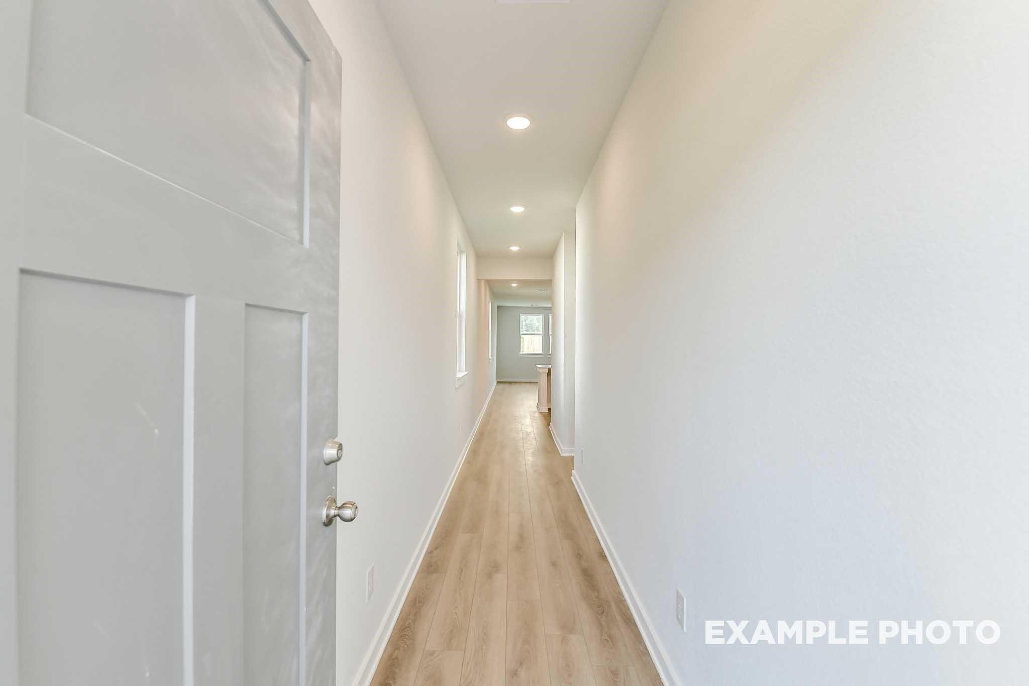 Bright hallway with white walls, recessed lights, hardwood floors, and open door in Davidson Homes The Colorado G, Conroe, Texas