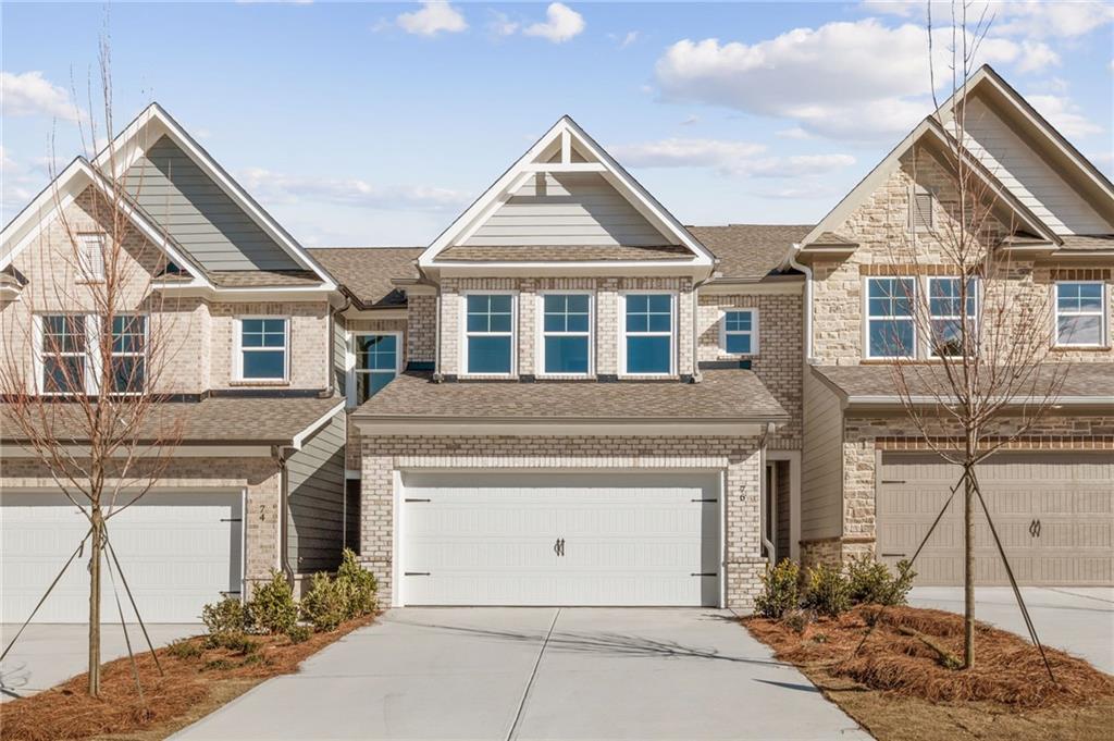 Three 2-story townhomes with beige brick facades, 2-car garages, and driveways in Lake Shore, Winder, Georgia by Davidson Homes