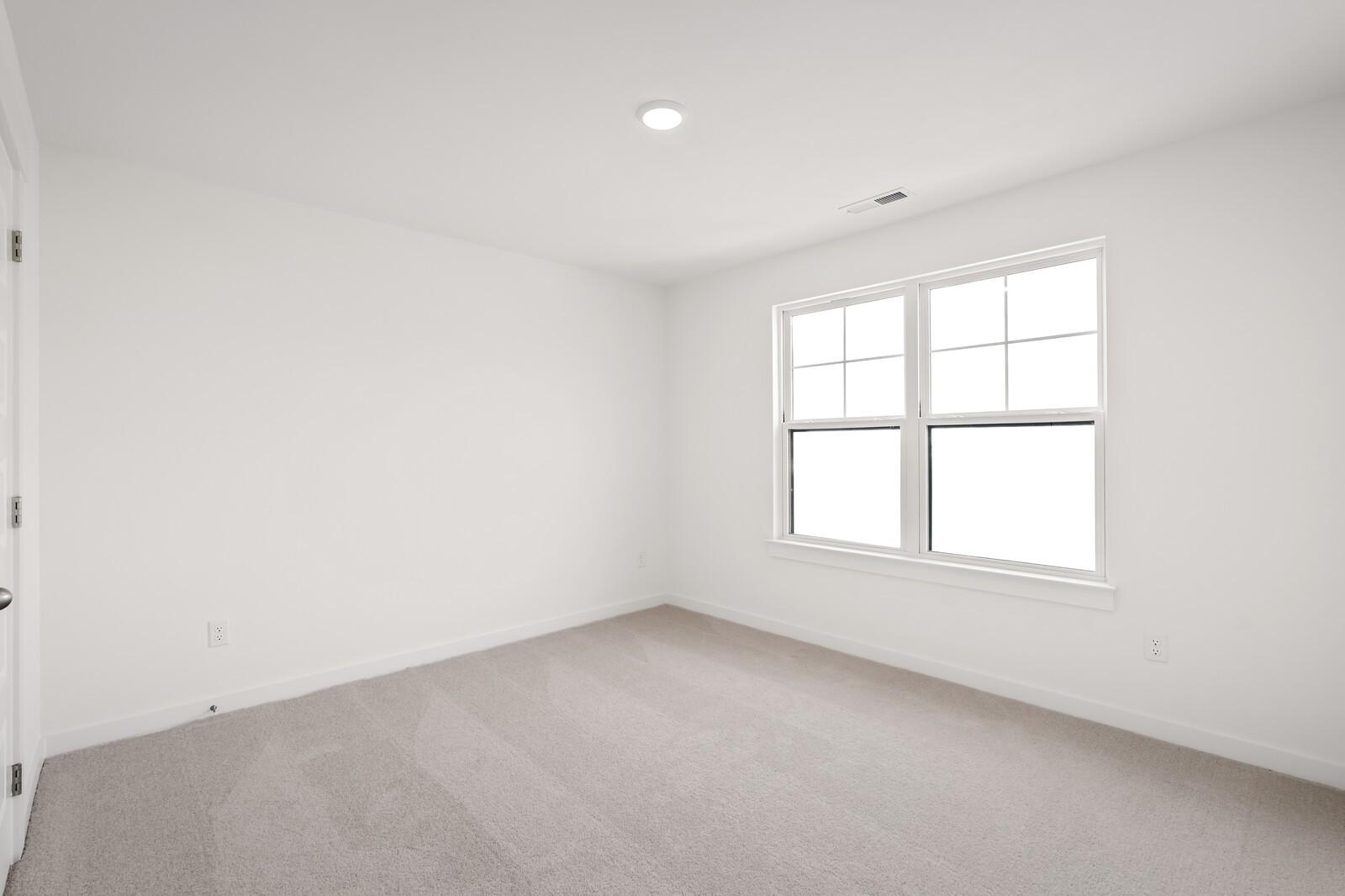 Bright empty bedroom with neutral carpet, white walls, and large double window in Davidson Homes The Ash C, Mt. Juliet, TN