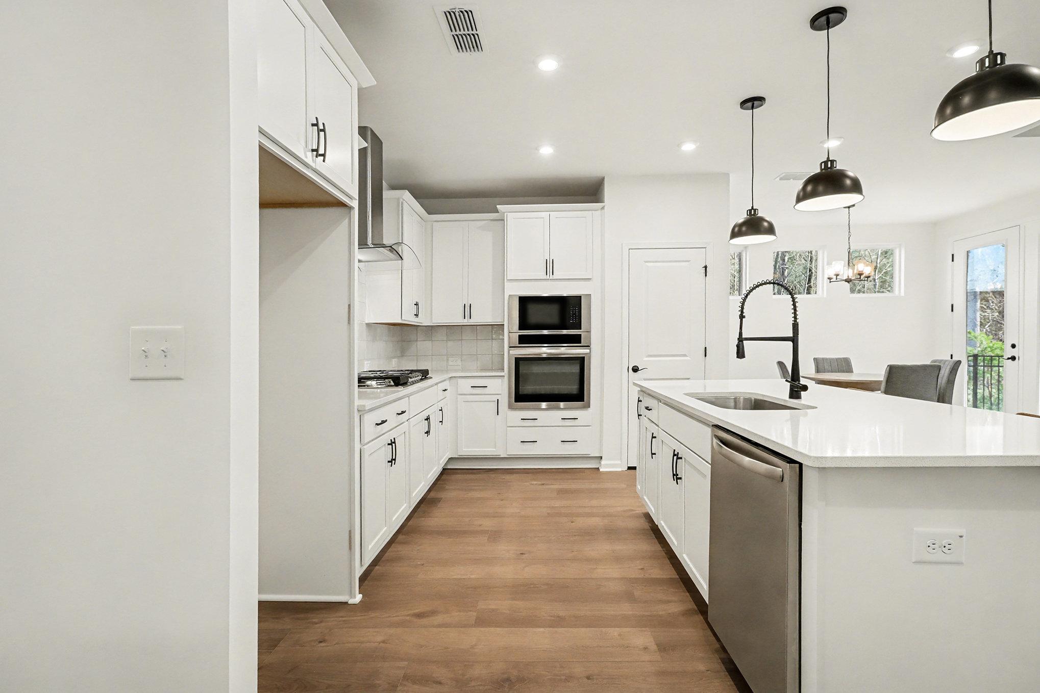 Modern white shaker kitchen with stainless double ovens, gas range, island sink, and pendant lights in Davidson Homes The Daphne B, Loganville, GA