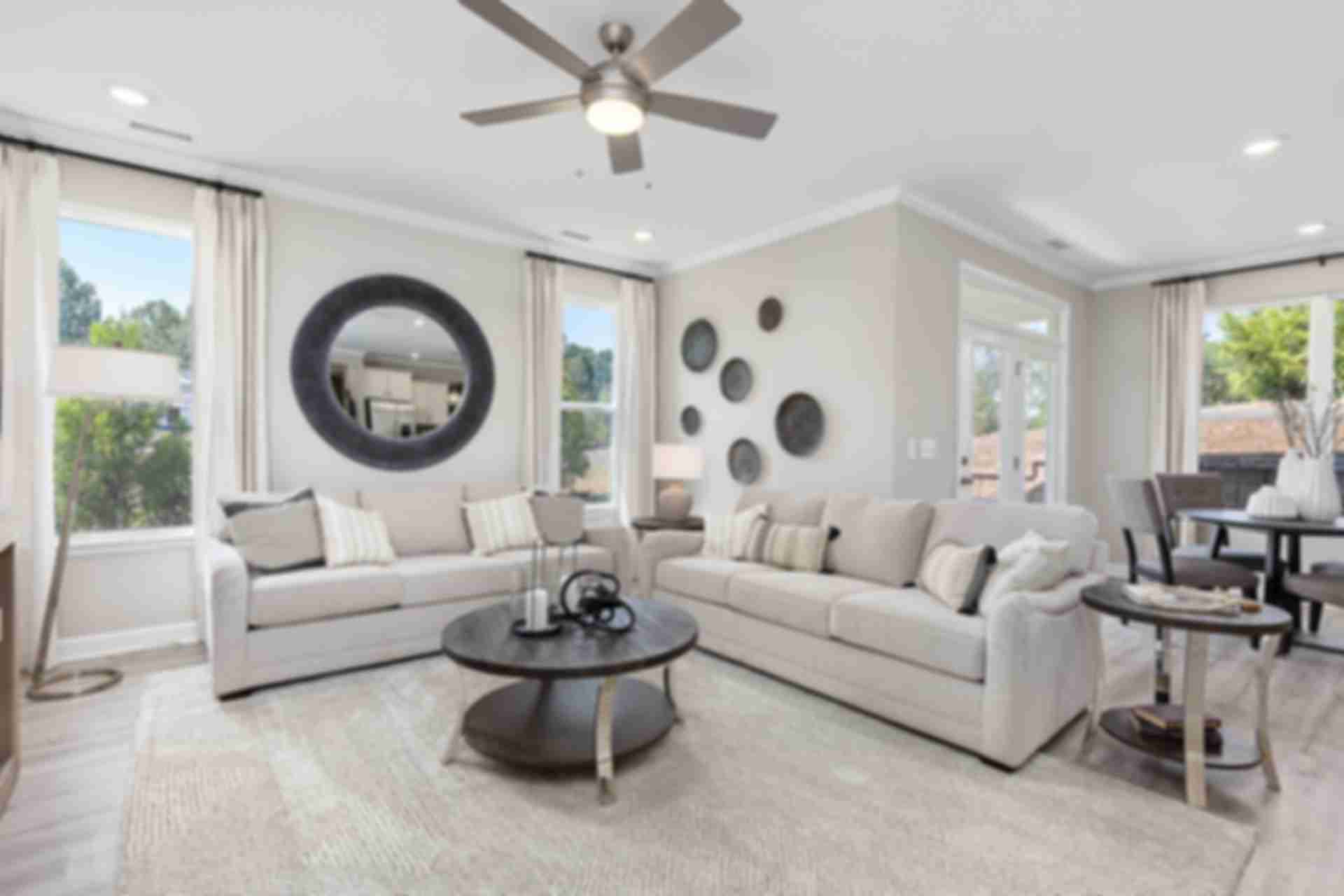 Spacious living room at Adams Vineyards in Fuquay-Varina NC with neutral sofas, round mirror, and large windows by Davidson Homes