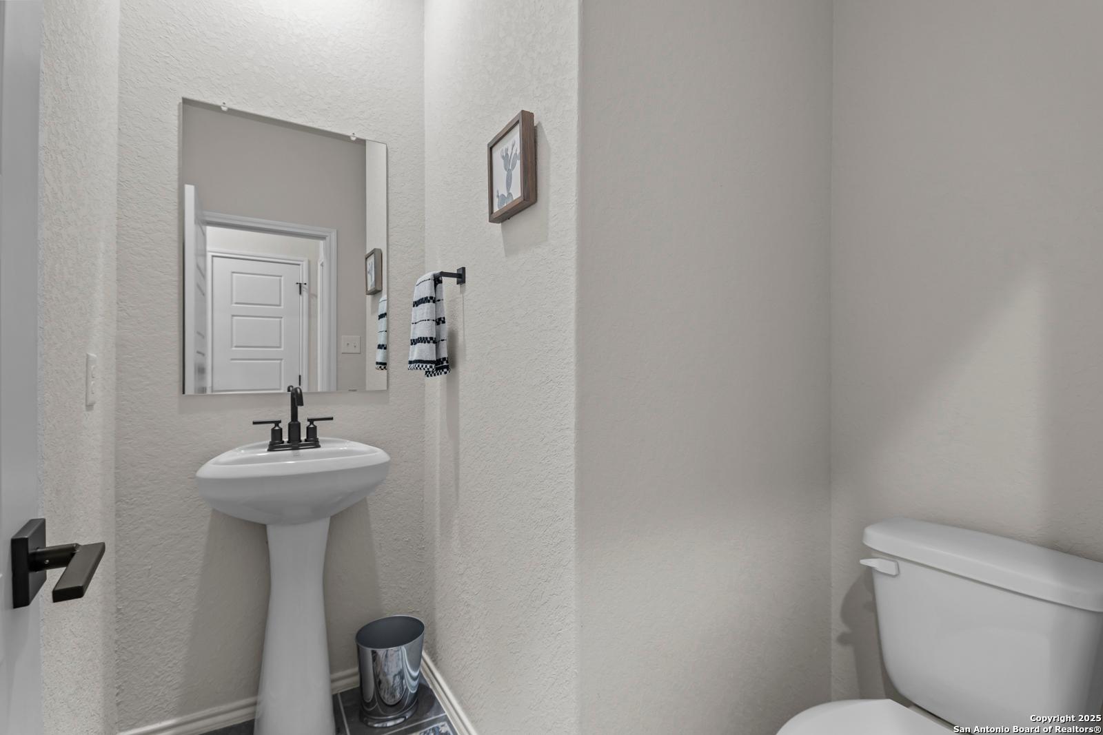 Elegant powder room featuring pedestal sink, framed mirror, and toilet in Davidson Homes The Douglas C, Seguin, Texas