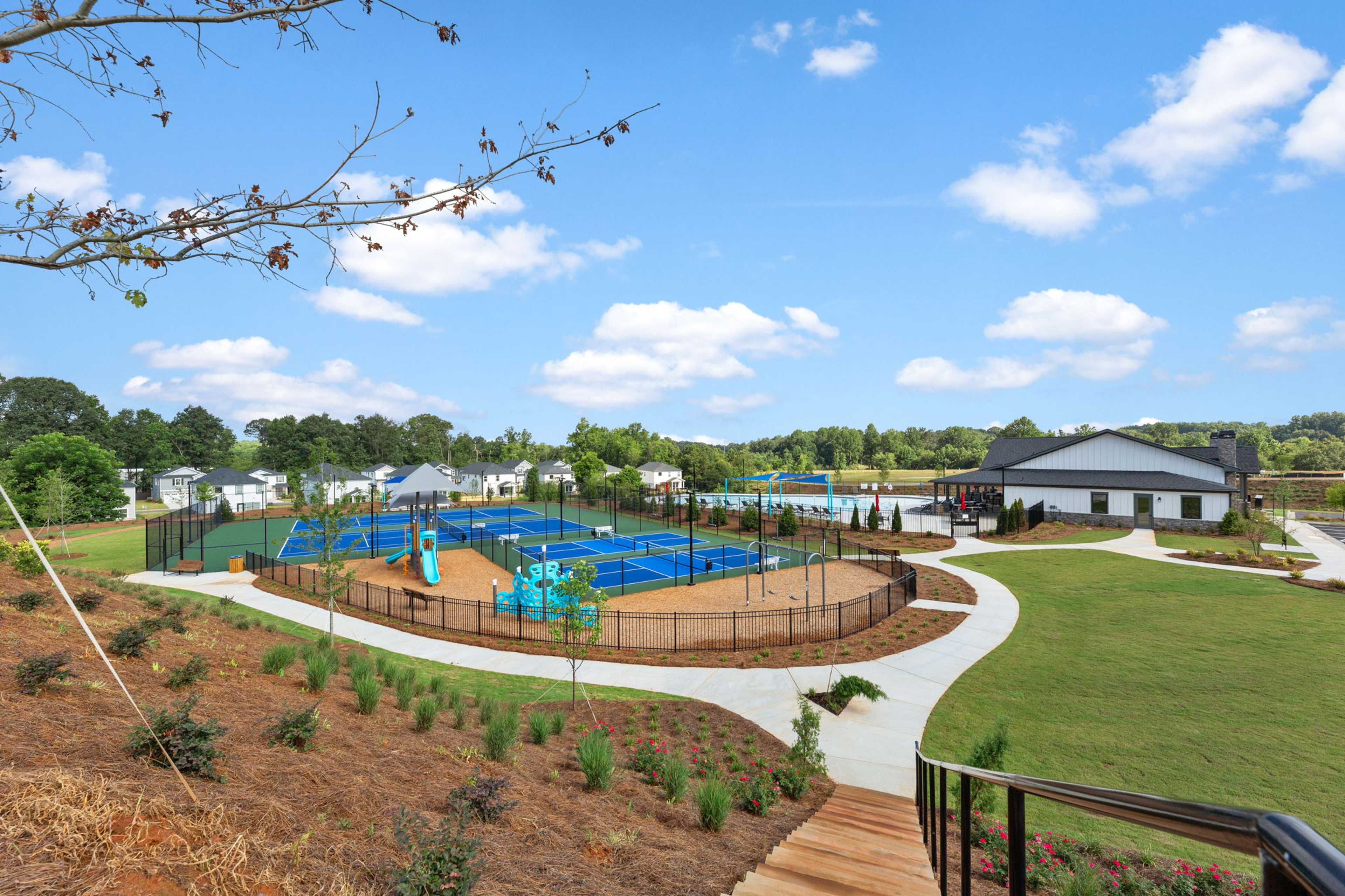 Fenced pickleball courts and colorful playground at Hemingway community in Cumming Georgia with clubhouse and lush landscaping