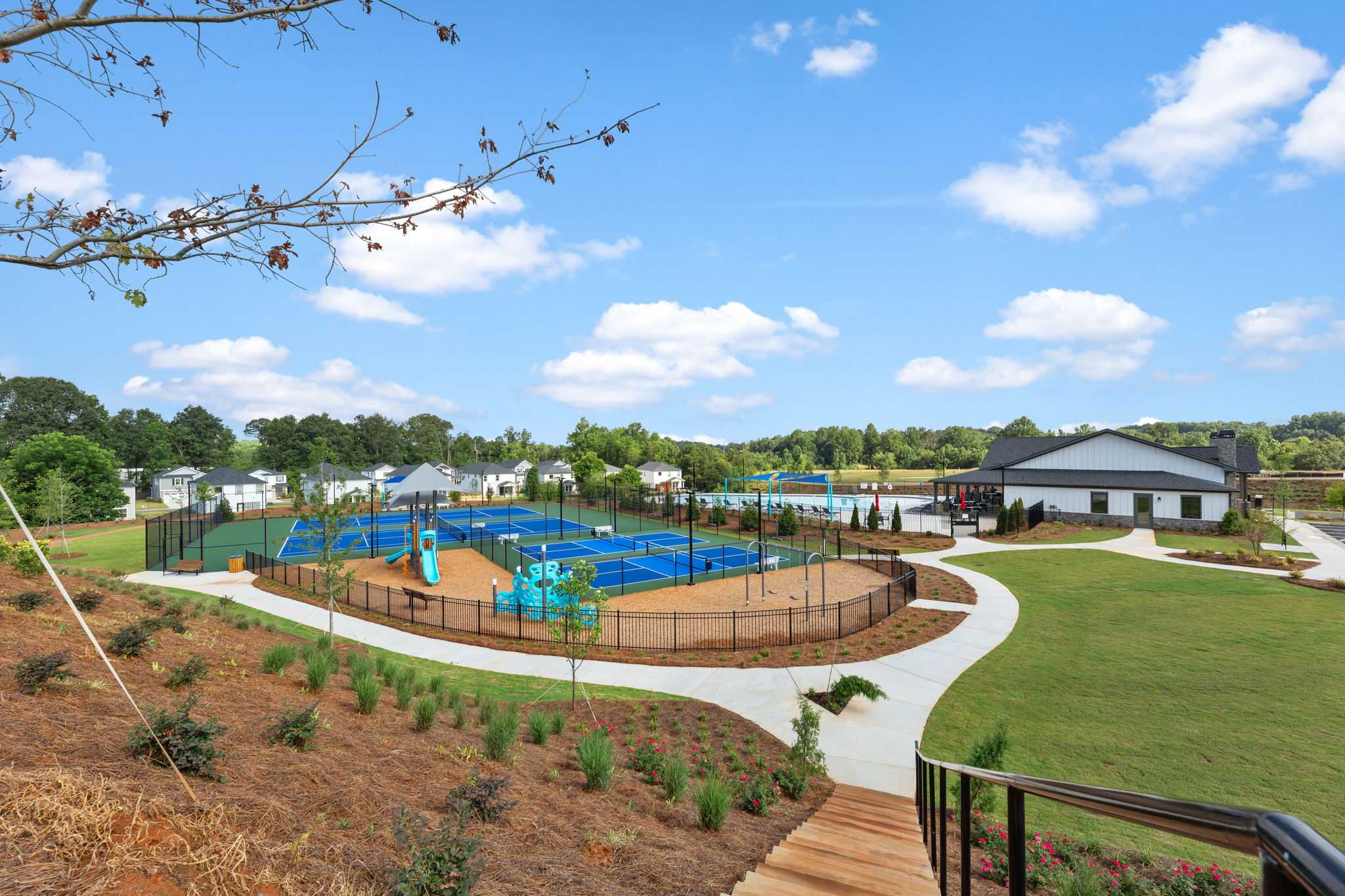 Fenced pickleball courts and colorful playground at Hemingway community in Cumming Georgia with clubhouse and lush landscaping