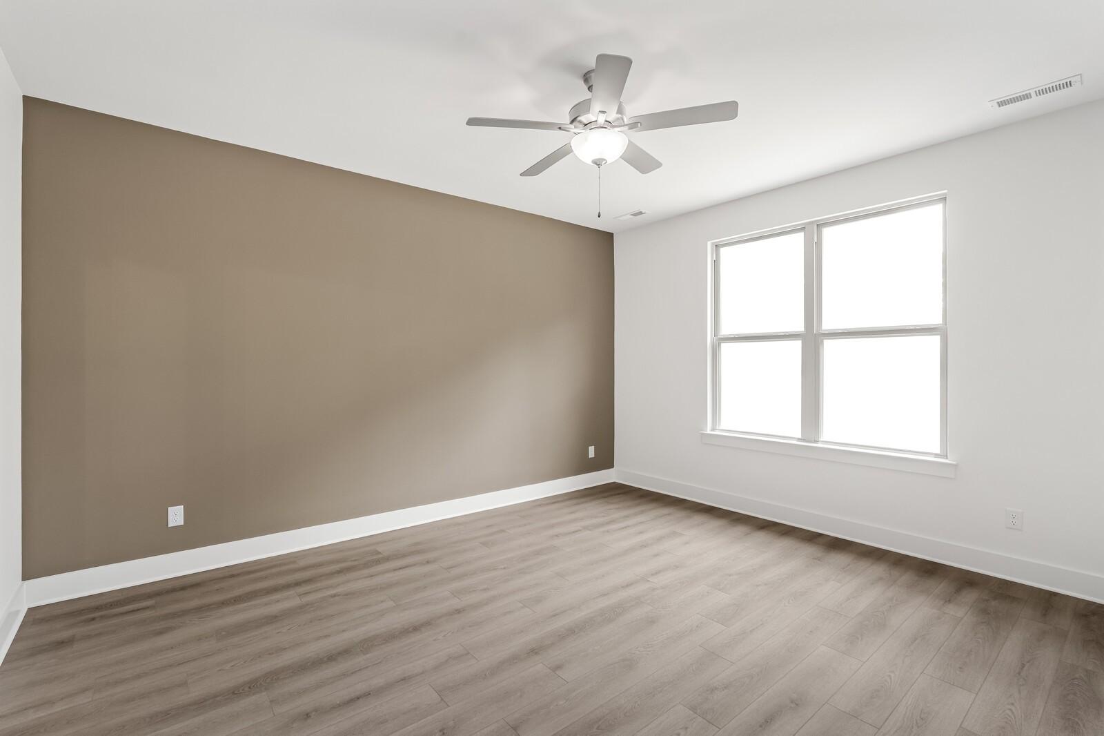 Spacious bedroom with wood-look flooring and accent wall in The Ridgeport C floor plan at Woods Crossing, Gallatin, TN.