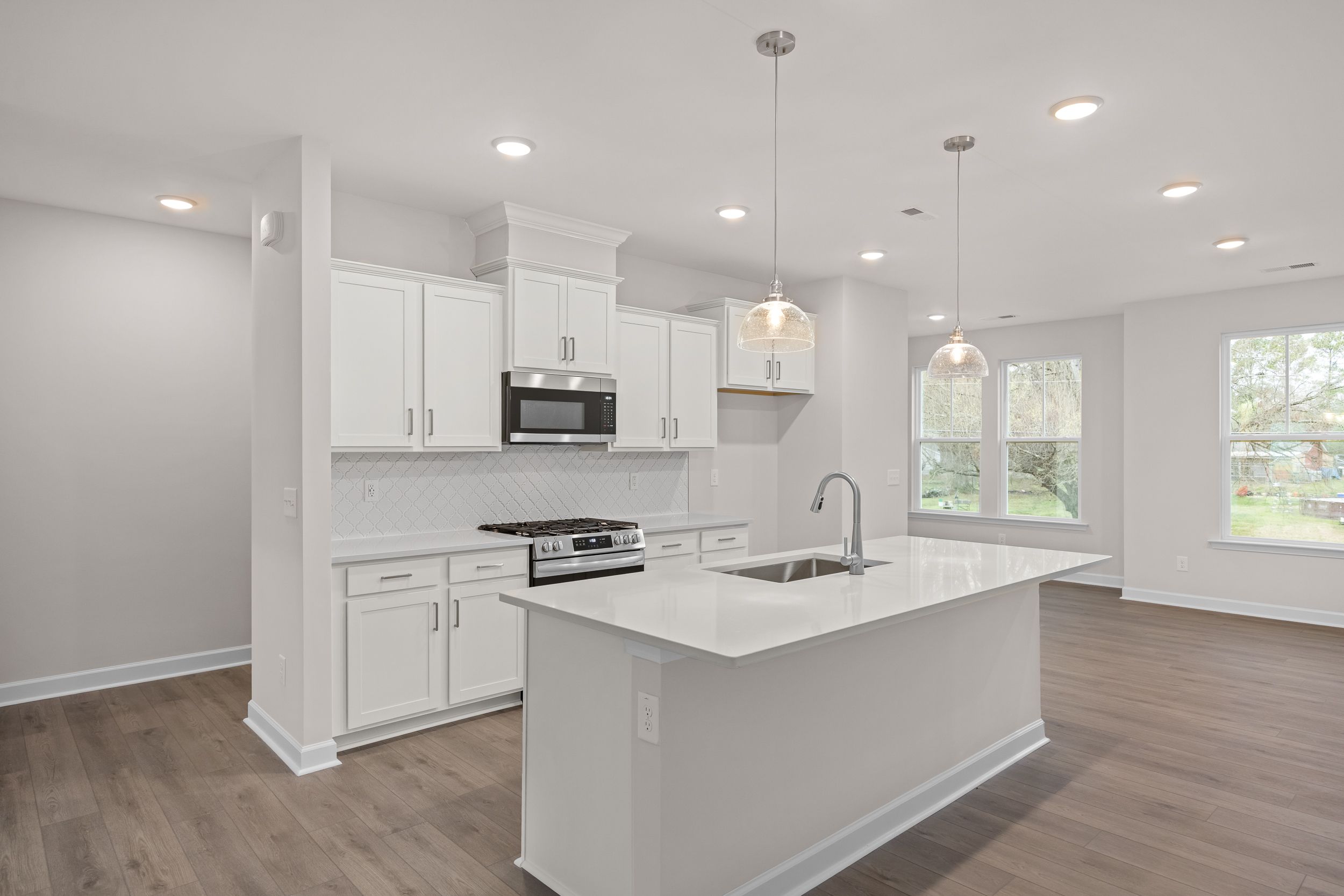 Bright kitchen at Forestville Yard Townhomes in Knightdale, NC with white cabinets, quartz island, stainless appliances, and hardwood floors