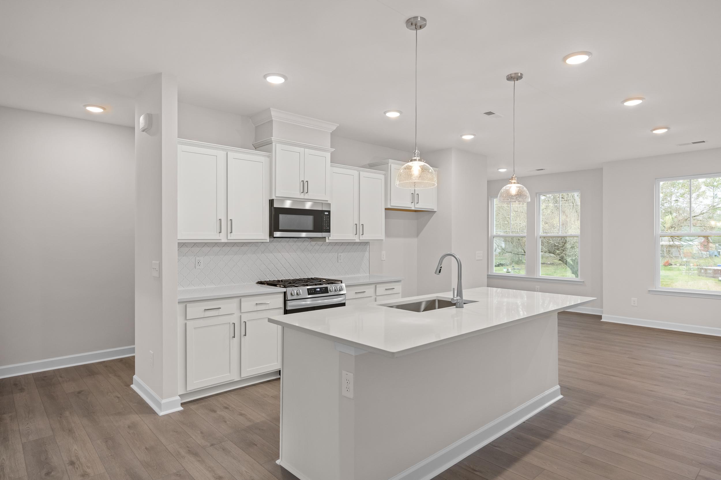 Bright kitchen at Forestville Yard Townhomes in Knightdale, NC with white cabinets, quartz island, stainless appliances, and hardwood floors