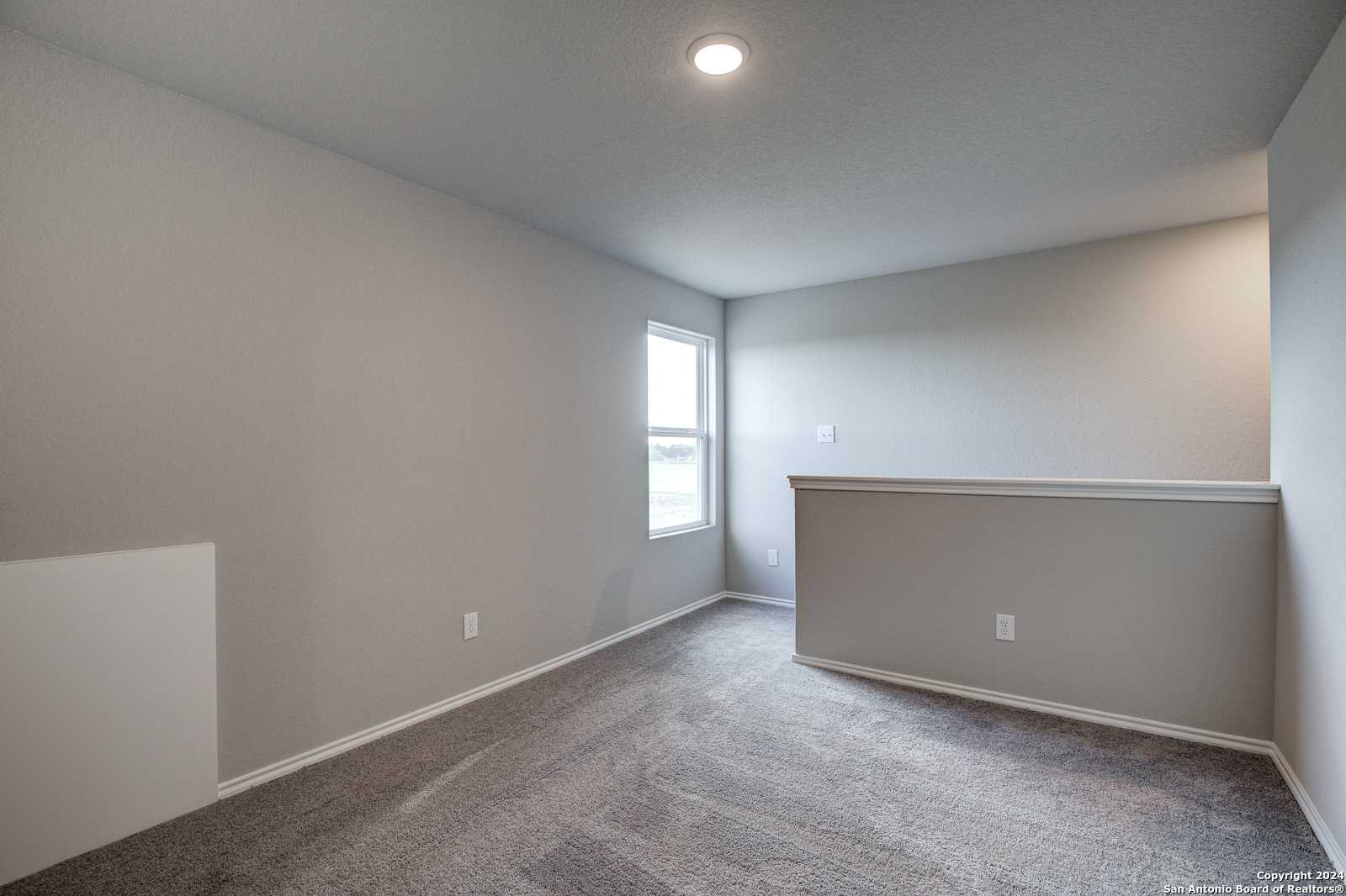 Spacious empty bedroom with light gray walls, carpet flooring, large window, and loft railing in Davidson Homes The Blanco C, San Antonio