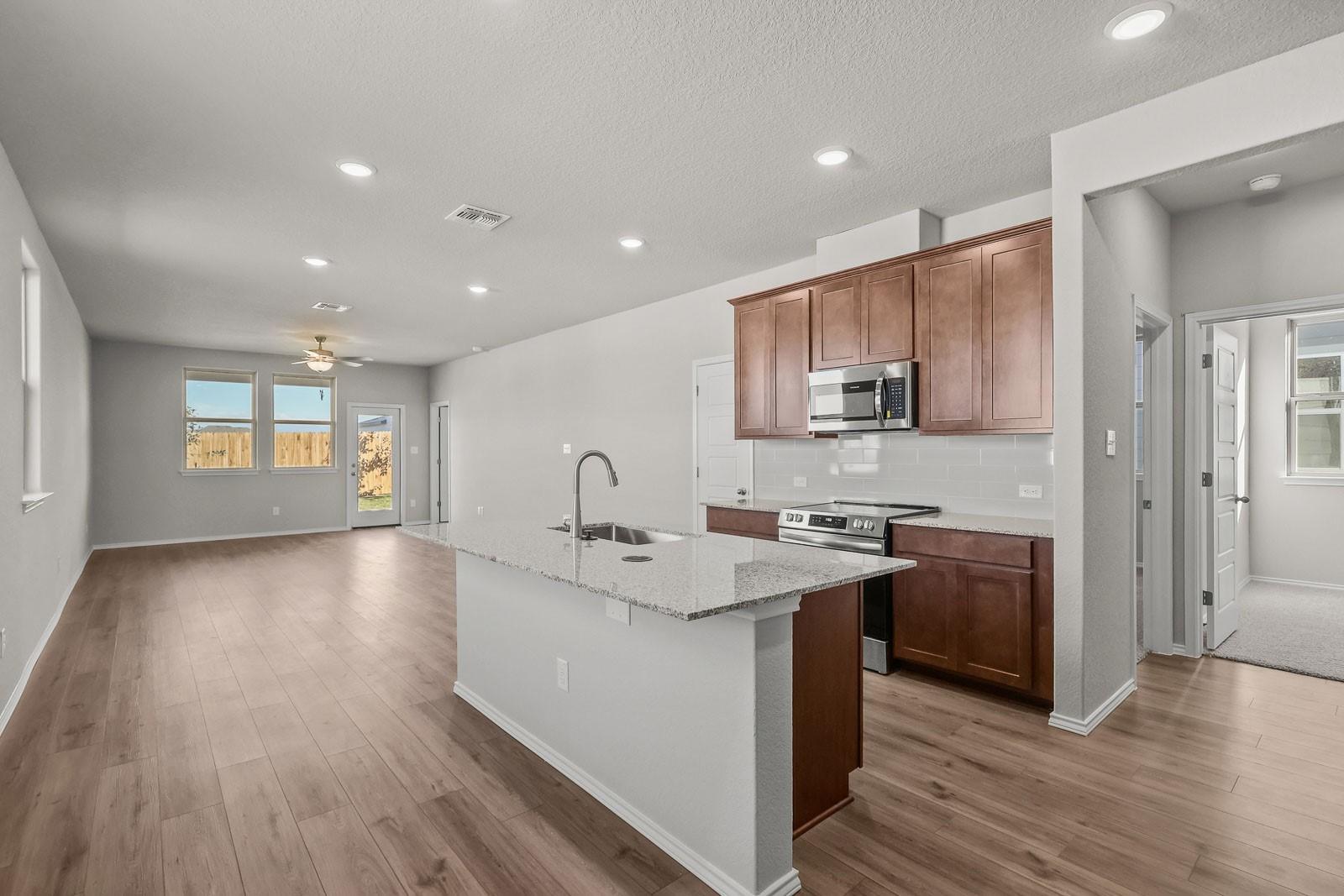 Open-concept kitchen with granite island and wood cabinetry in The Frio G floor plan by Davidson Homes in Heartland, TX.