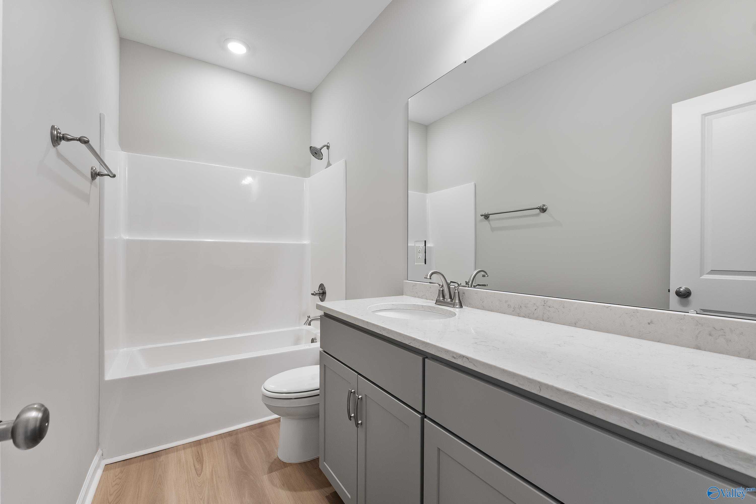 Modern bathroom featuring white tub-shower combo, quartz vanity with gray cabinets, and chrome fixtures in Evermore Homes The Grace, Madison, Alabama
