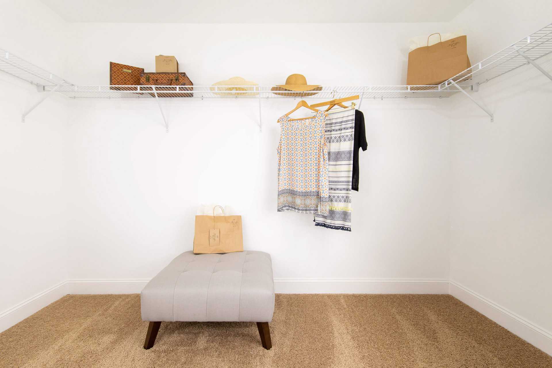 Spacious walk-in closet at Summer Pointe in Madison, Alabama with wire shelving, hanging apparel, hats, luggage, and gray ottoman