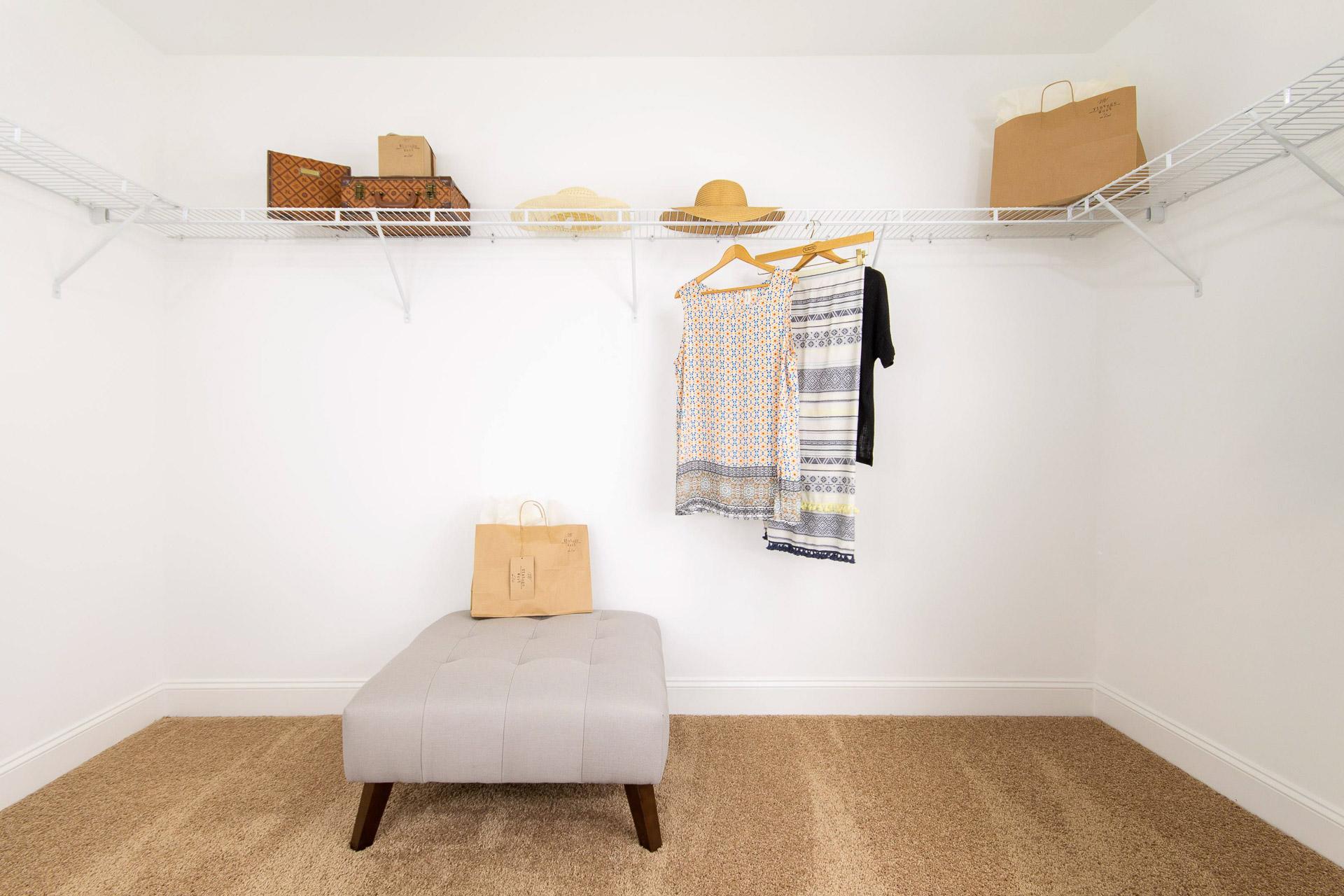Spacious walk-in closet at Summer Pointe in Madison, Alabama with wire shelving, hanging apparel, hats, luggage, and gray ottoman