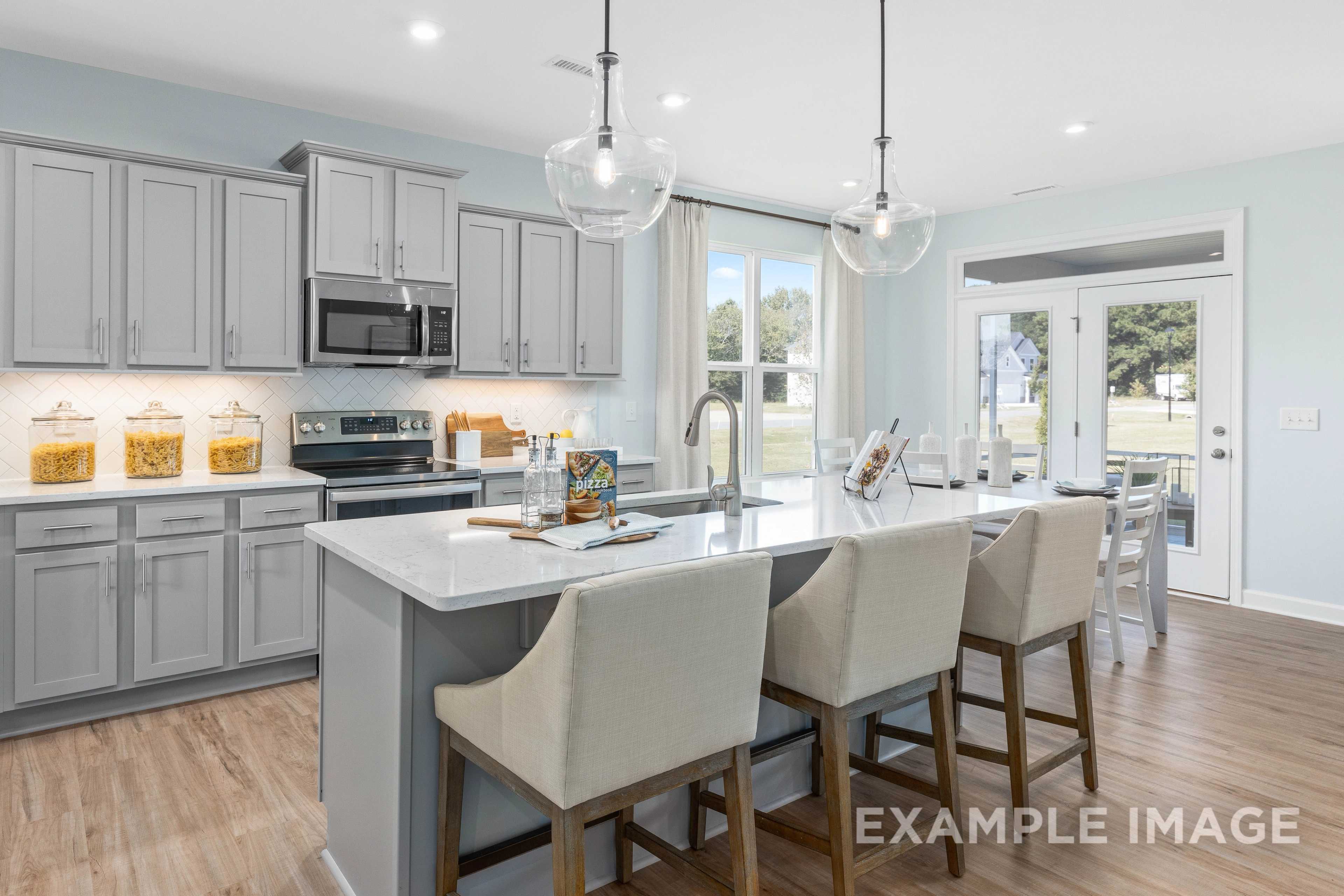Spacious kitchen in The Ash C home with gray shaker cabinets, quartz island, stainless appliances, and pendant lights