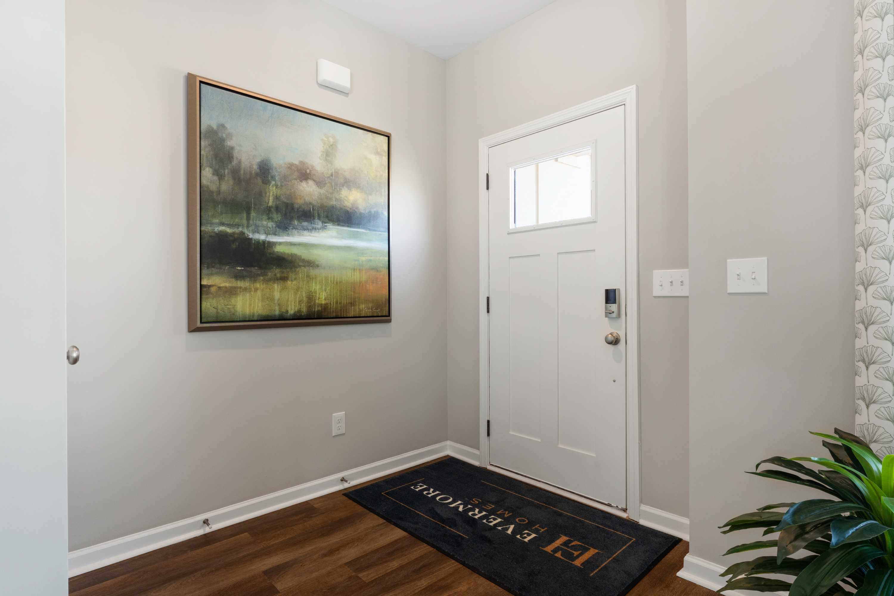 Entryway in Evergreen Mill home by Evermore Homes in Madison, Alabama with framed landscape painting, white door, and hardwood floors