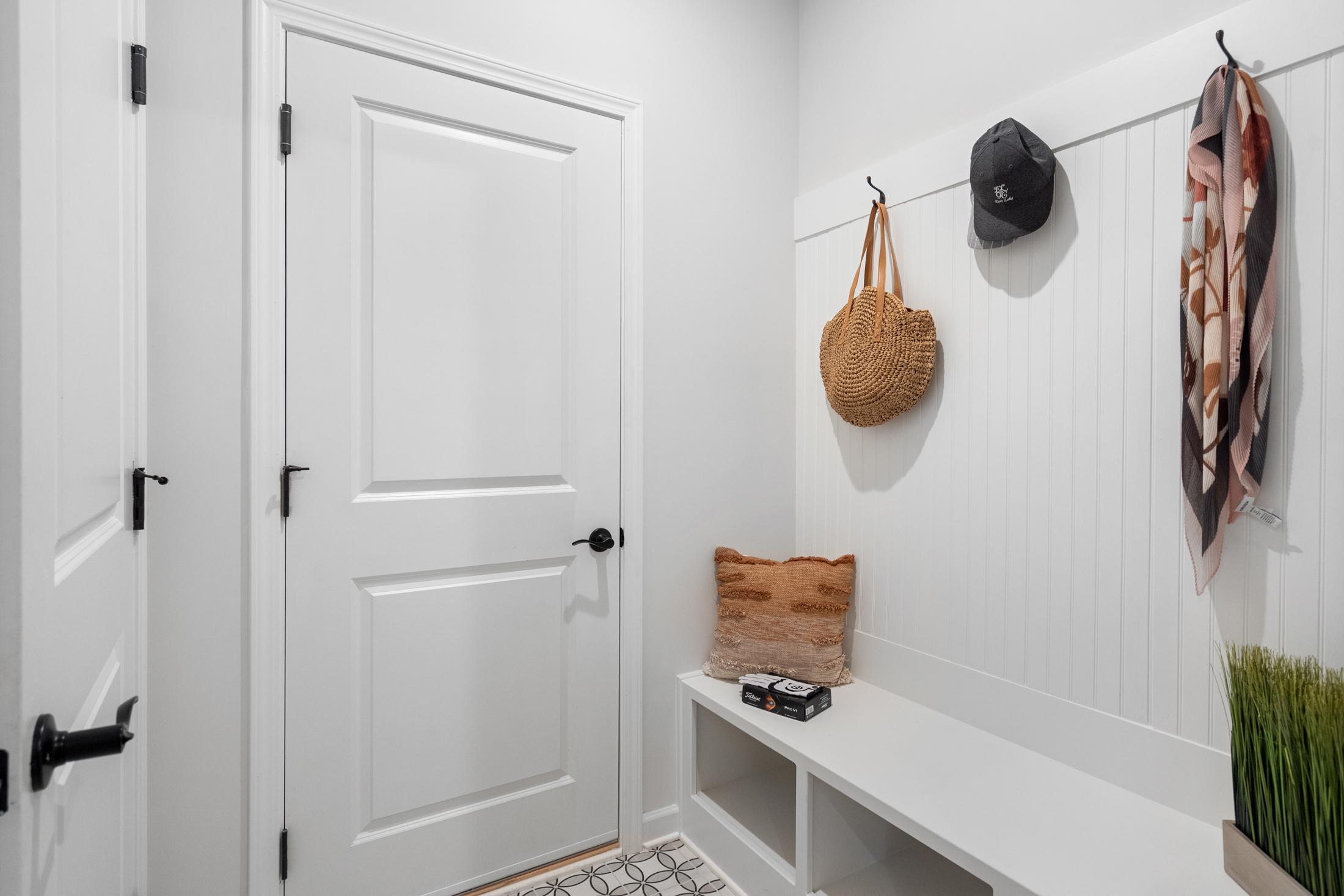 The Edison A mudroom featuring white wainscoting, built-in bench with cushion, coat hooks with hat scarf and bag, Loganville home