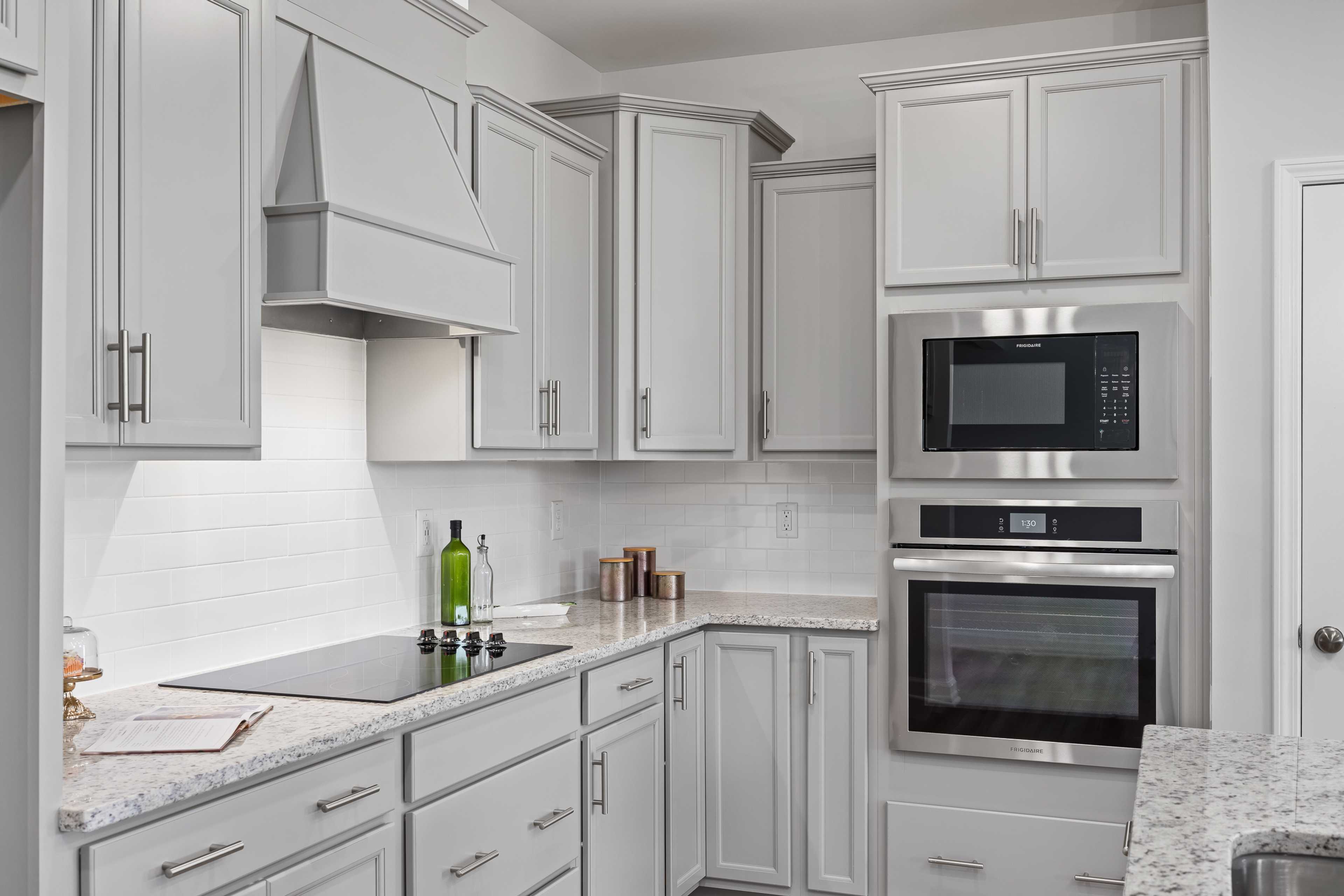 Modern white shaker kitchen with granite counters, stainless double oven, and subway tile backsplash at Woodland Crossing in Zebulon NC