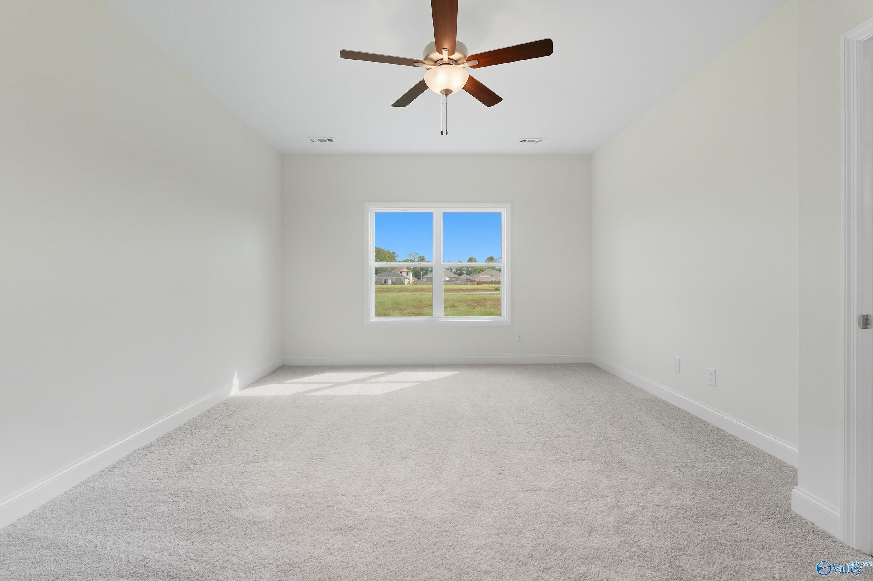 Bright empty bedroom with ceiling fan, beige carpet, and large window overlooking green yard in Davidson Homes The Everett, Meridianville, Alabama