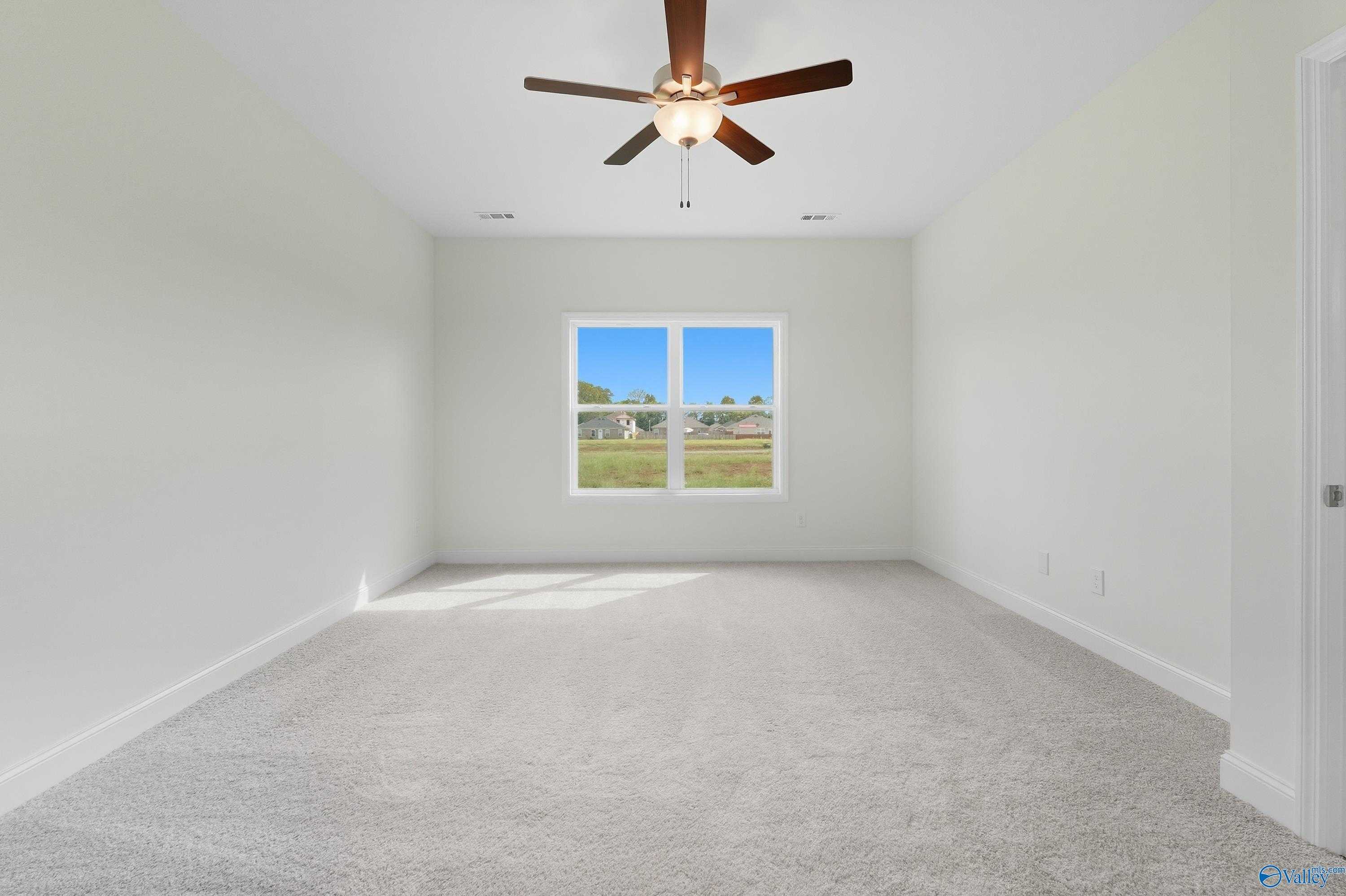 Spacious empty bedroom with beige carpet, ceiling fan, and large window view in Davidson Homes The Everett, Meridianville, Alabama