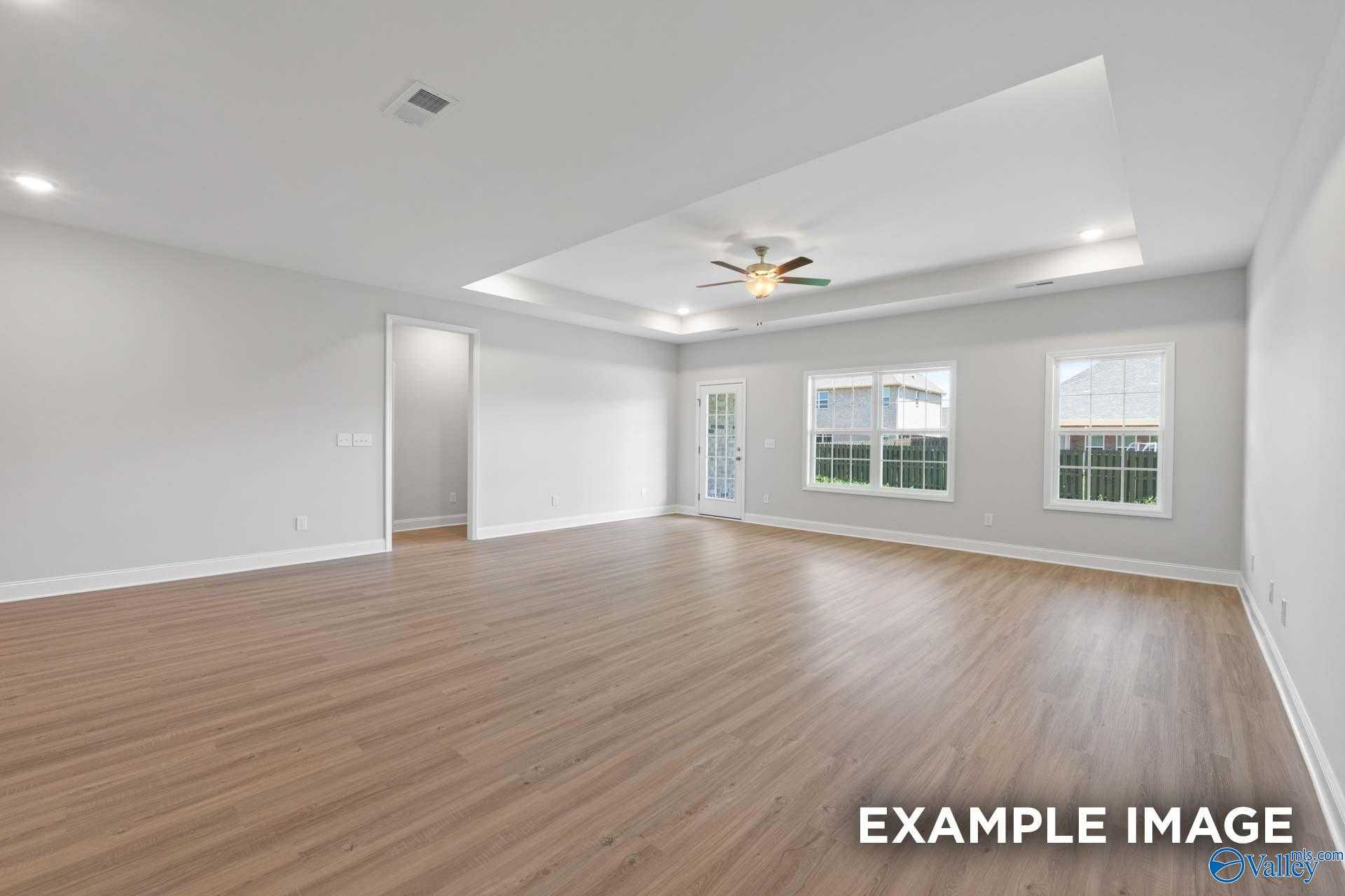 Spacious living room with hardwood floors, ceiling fan, French doors, and large windows in Davidson Homes The Lanier, Meridianville AL