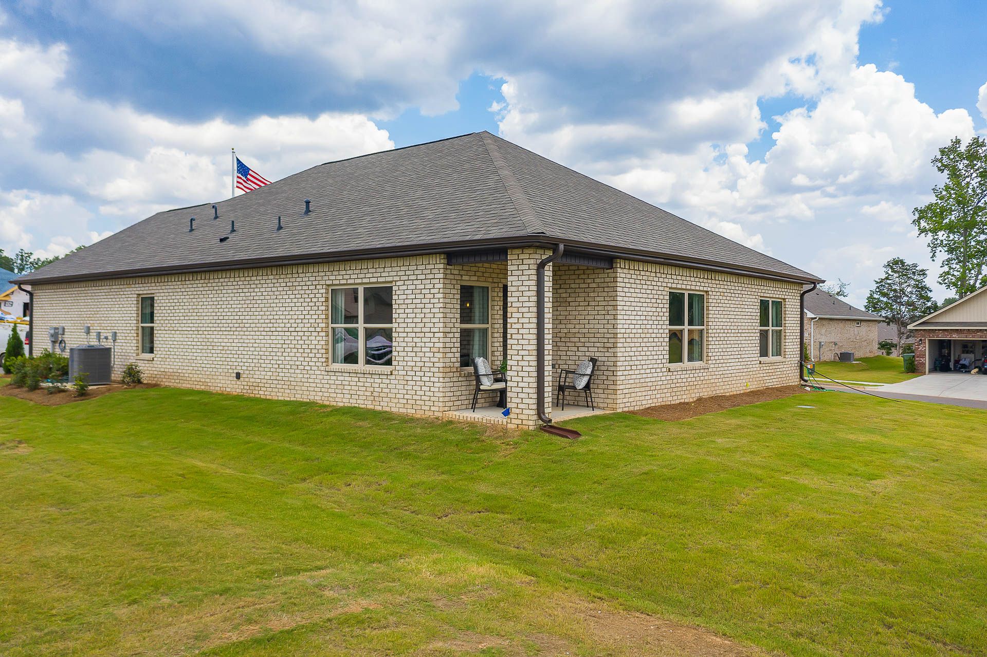 Beige brick home side exterior at Heritage Heights in Madison AL with small porch, chairs, American flag, and green lawn