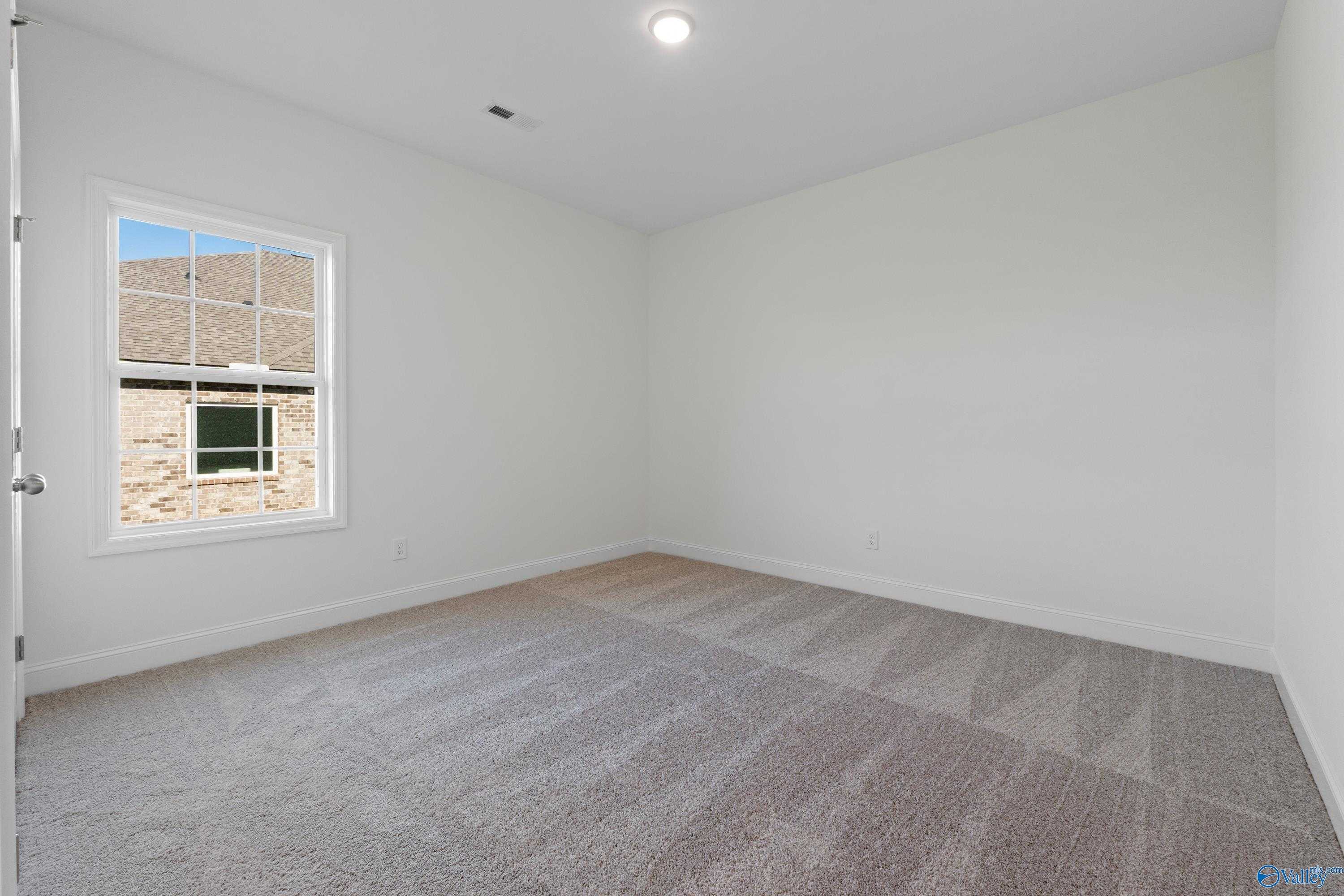 Bright secondary bedroom with large window, neutral carpet, and white walls in Davidson Homes The Oxford, Harvest, AL