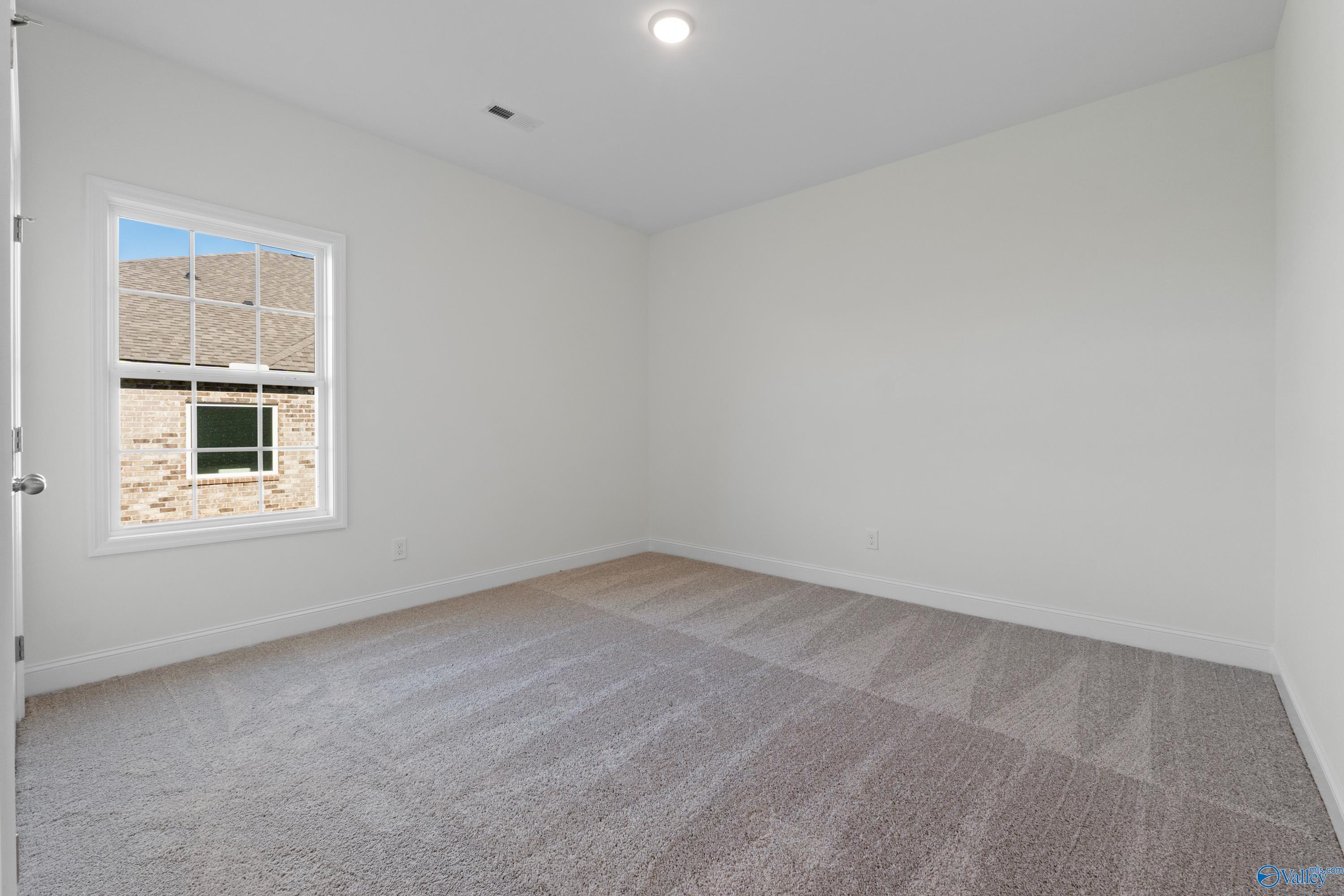 Bright secondary bedroom with large window, neutral carpet, and white walls in Davidson Homes The Oxford, Harvest, AL