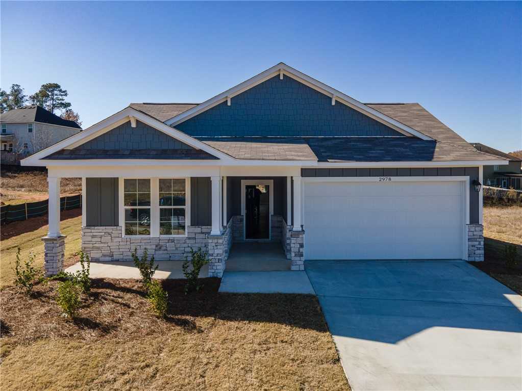 Modern 4-bedroom single-story home with blue-gray siding, stone accents, covered porch, and 2-car garage in Anderson Lakes, Opelika