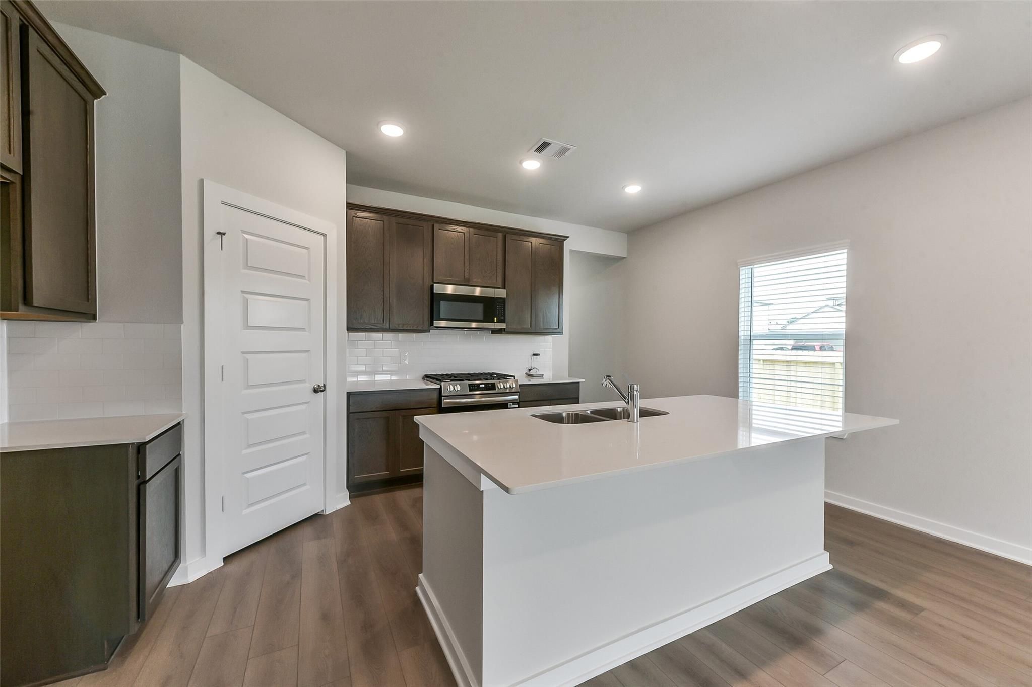Modern kitchen featuring brown cabinets, white quartz island with sink, stainless appliances in The Sabine F by Davidson Homes, Dayton, Texas