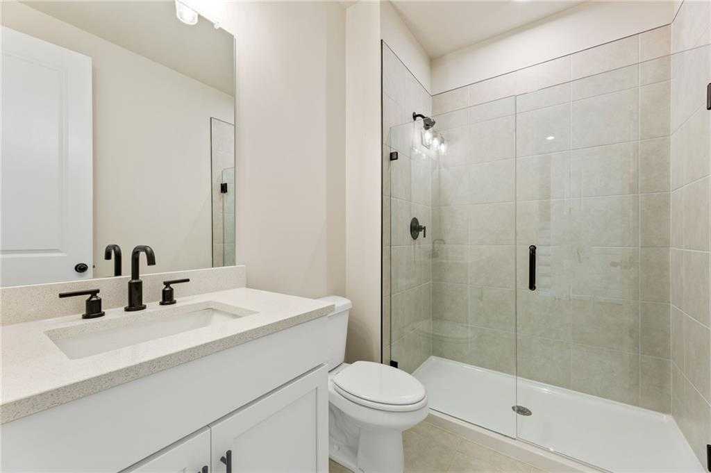 Modern master bathroom with frameless glass shower, white quartz vanity, black fixtures, and subway tile in The Hickory E, Buford, GA