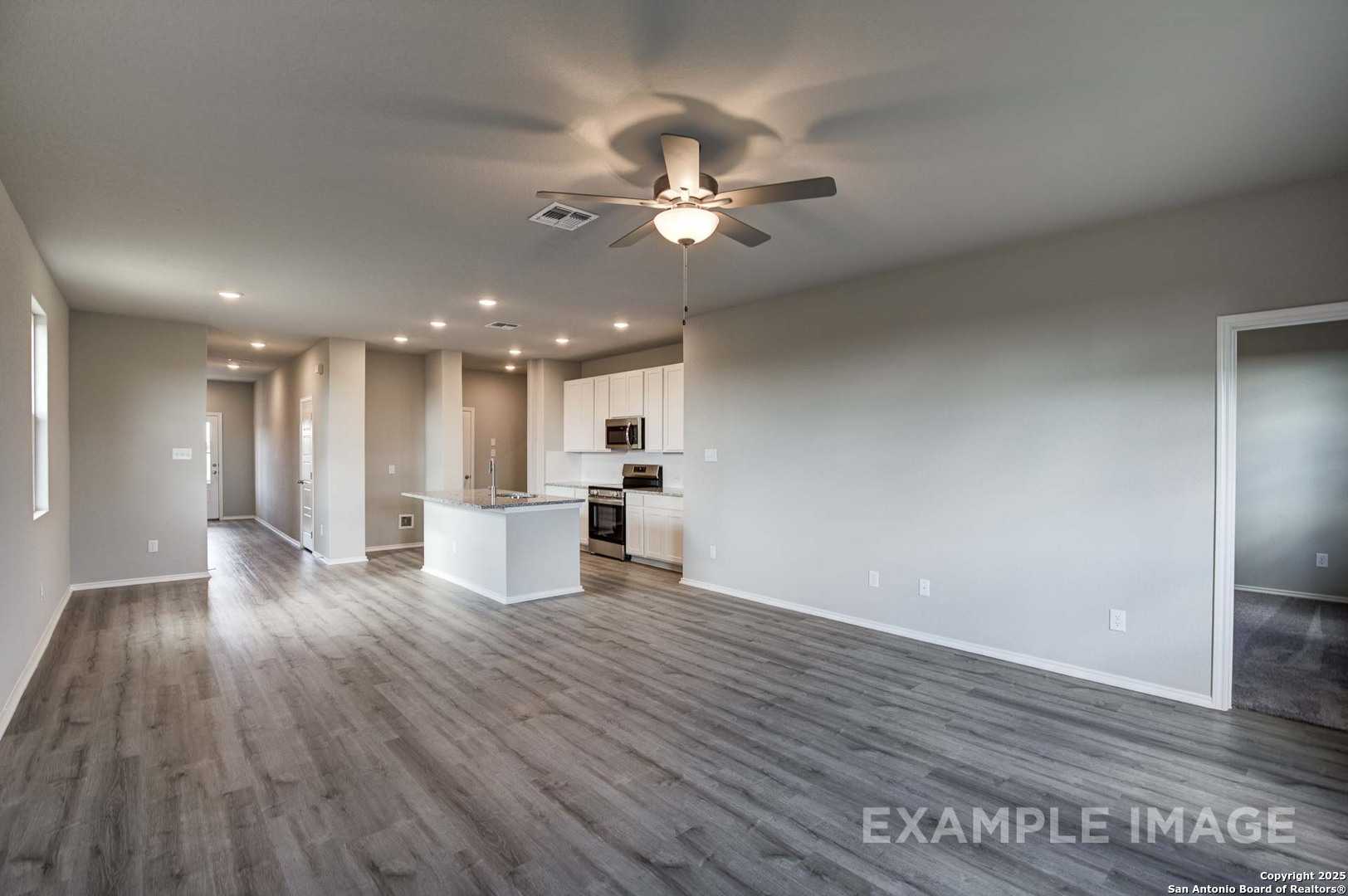 Open-concept kitchen with white cabinets, center island, and luxury vinyl plank floors in Davidson Homes The Blanco C, Agave, San Antonio