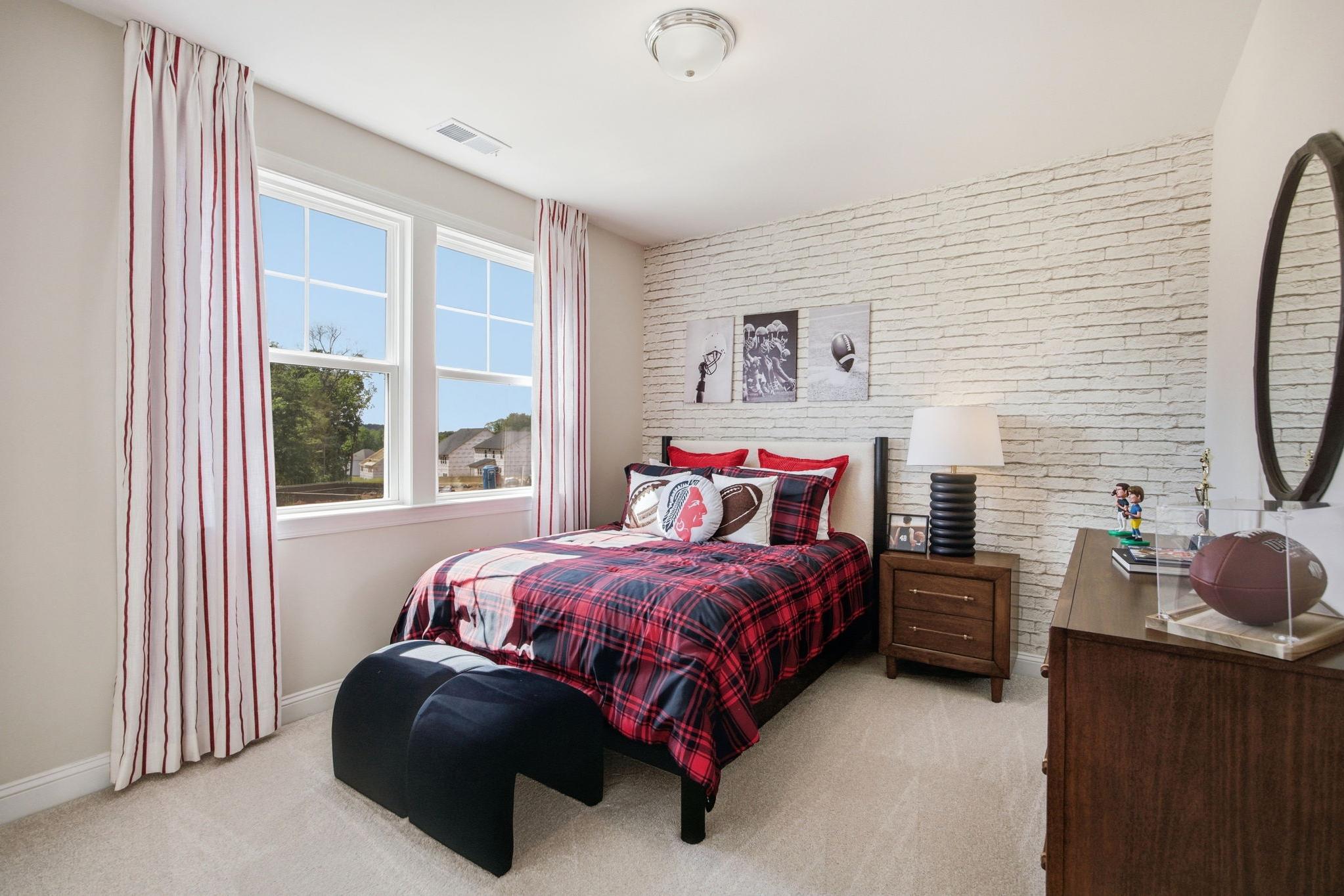Boy's sports-themed bedroom at Enclave at Belmont in Belmont NC with plaid bedding, football decor, white brick wall, and large windows