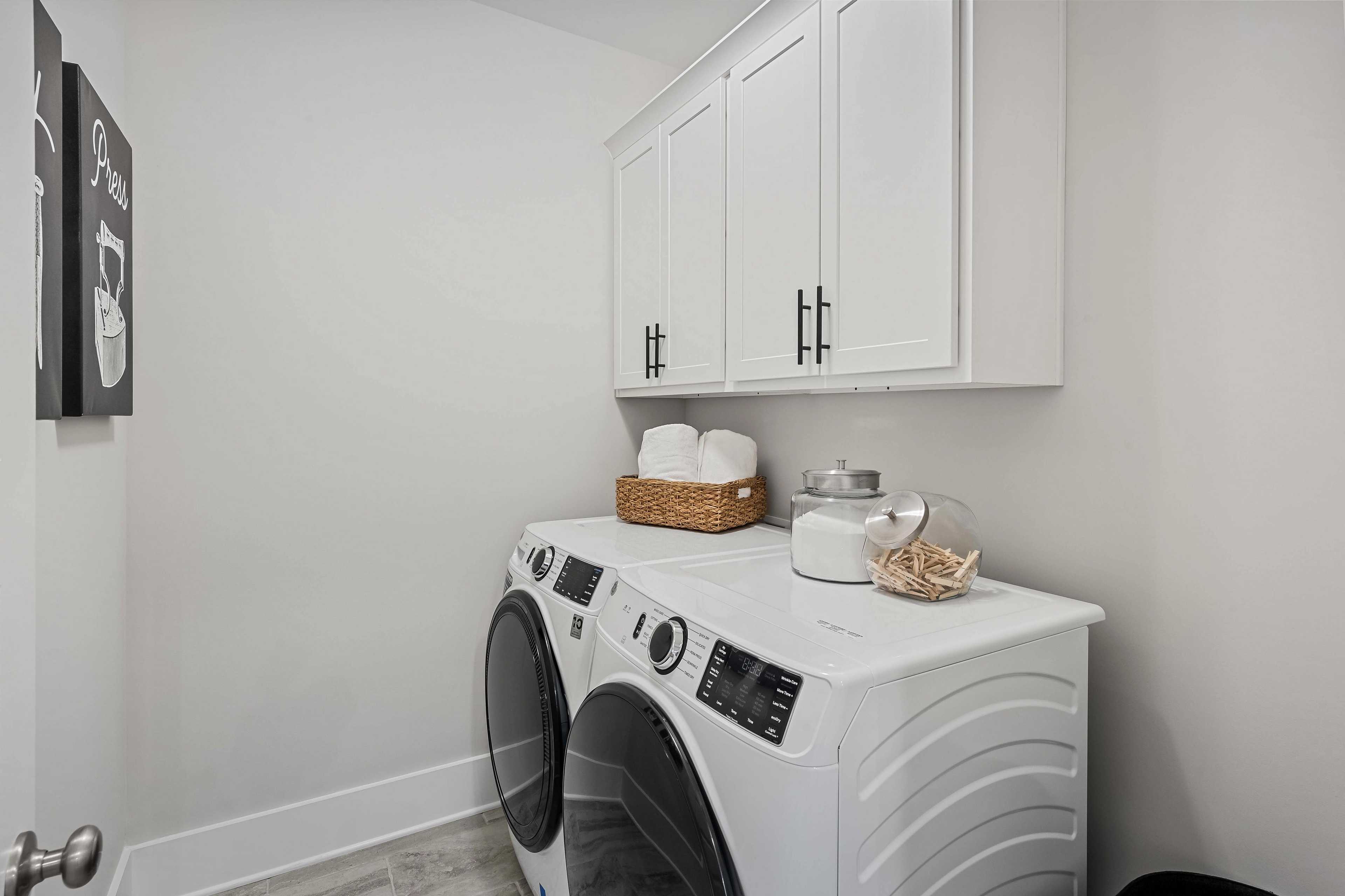 Modern laundry room at Cain Park in Hartselle Alabama with white front-load washer dryer upper cabinets and towel basket