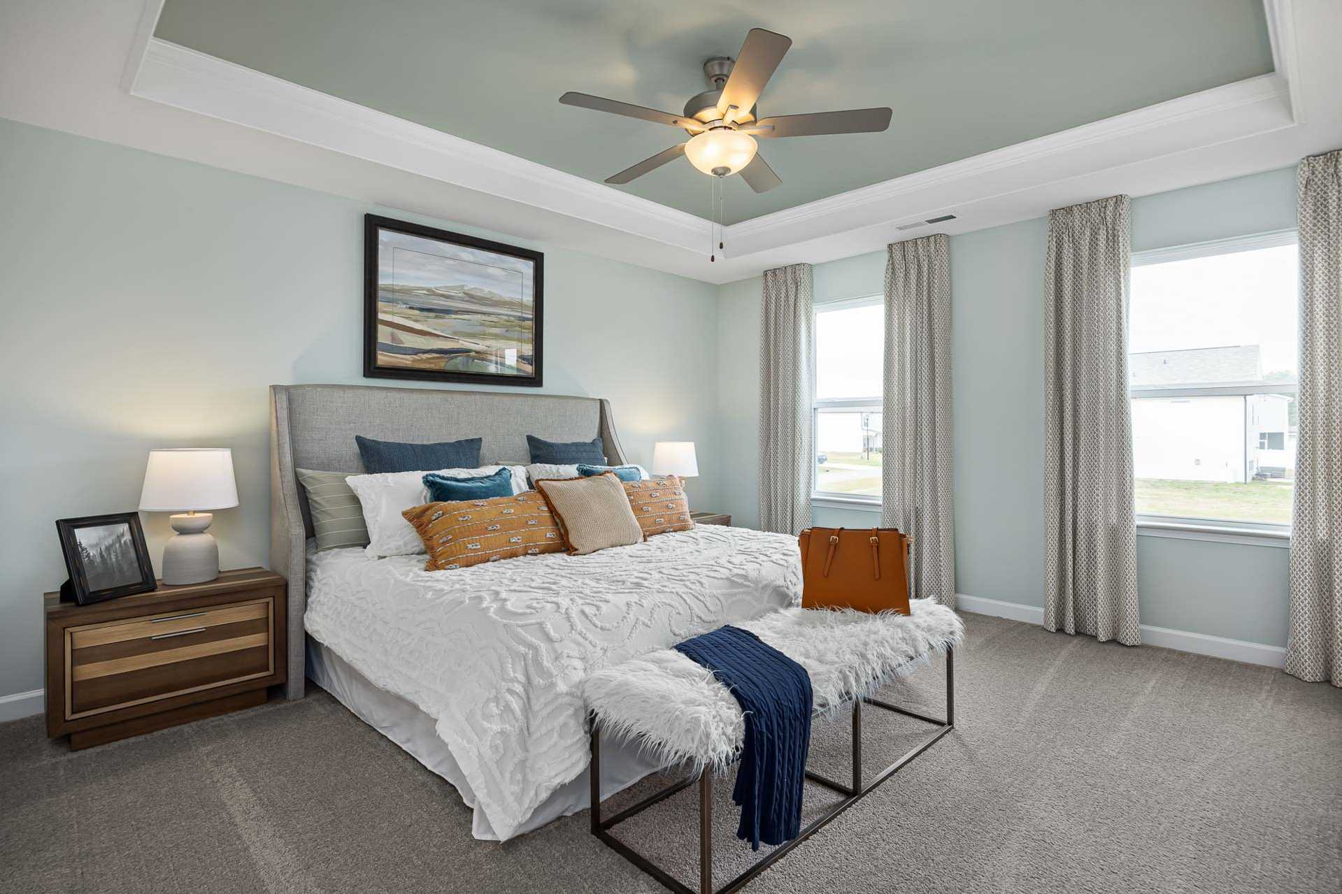 Serene master bedroom at Beverly Place in Four Oaks NC featuring king bed, ceiling fan, and large windows by Davidson Homes